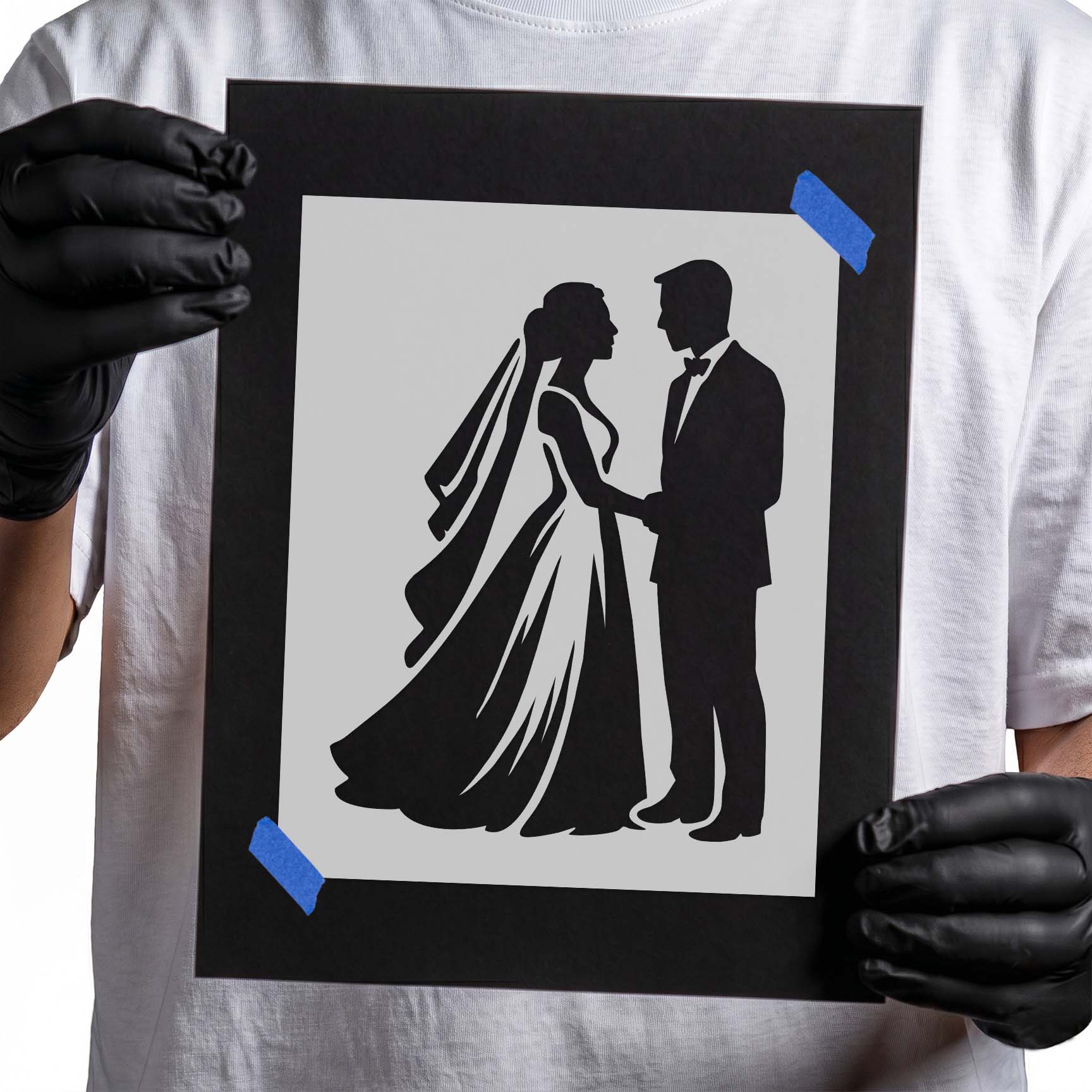 Gloved hands holding Bride & Groom Silhouette Stencil taped to black cardboard