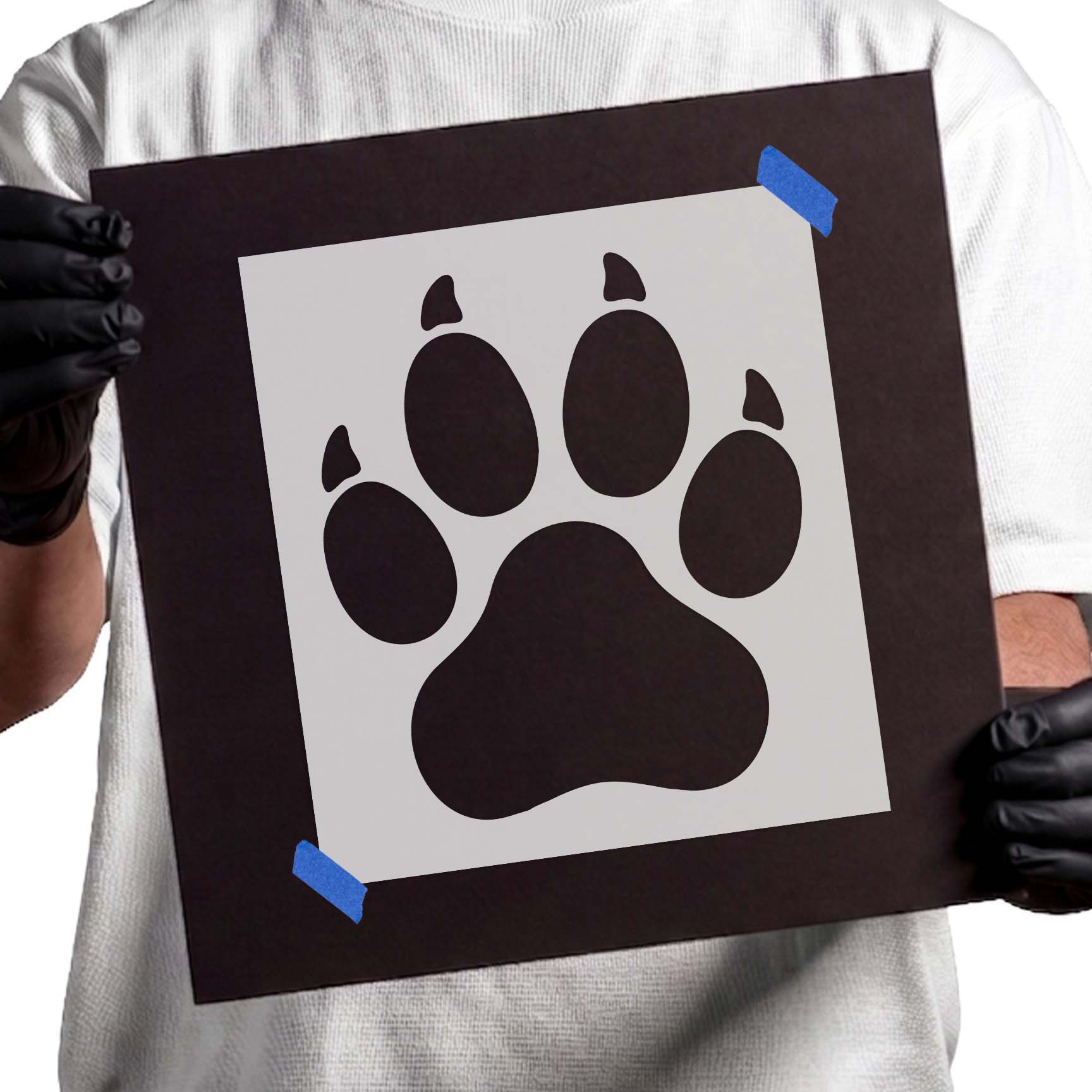 Gloved hands holding Clawed Paw Print Stencil taped to black cardboard