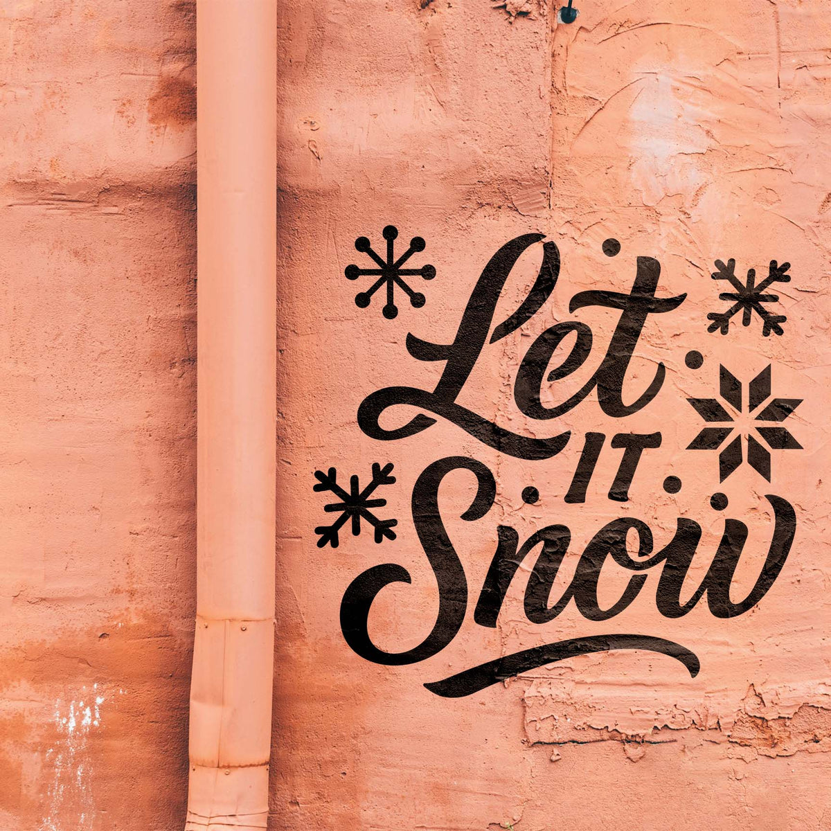 Black Festive Let It Snow Text Stencil stands out with playful snowflakes on a textured salmon wall.