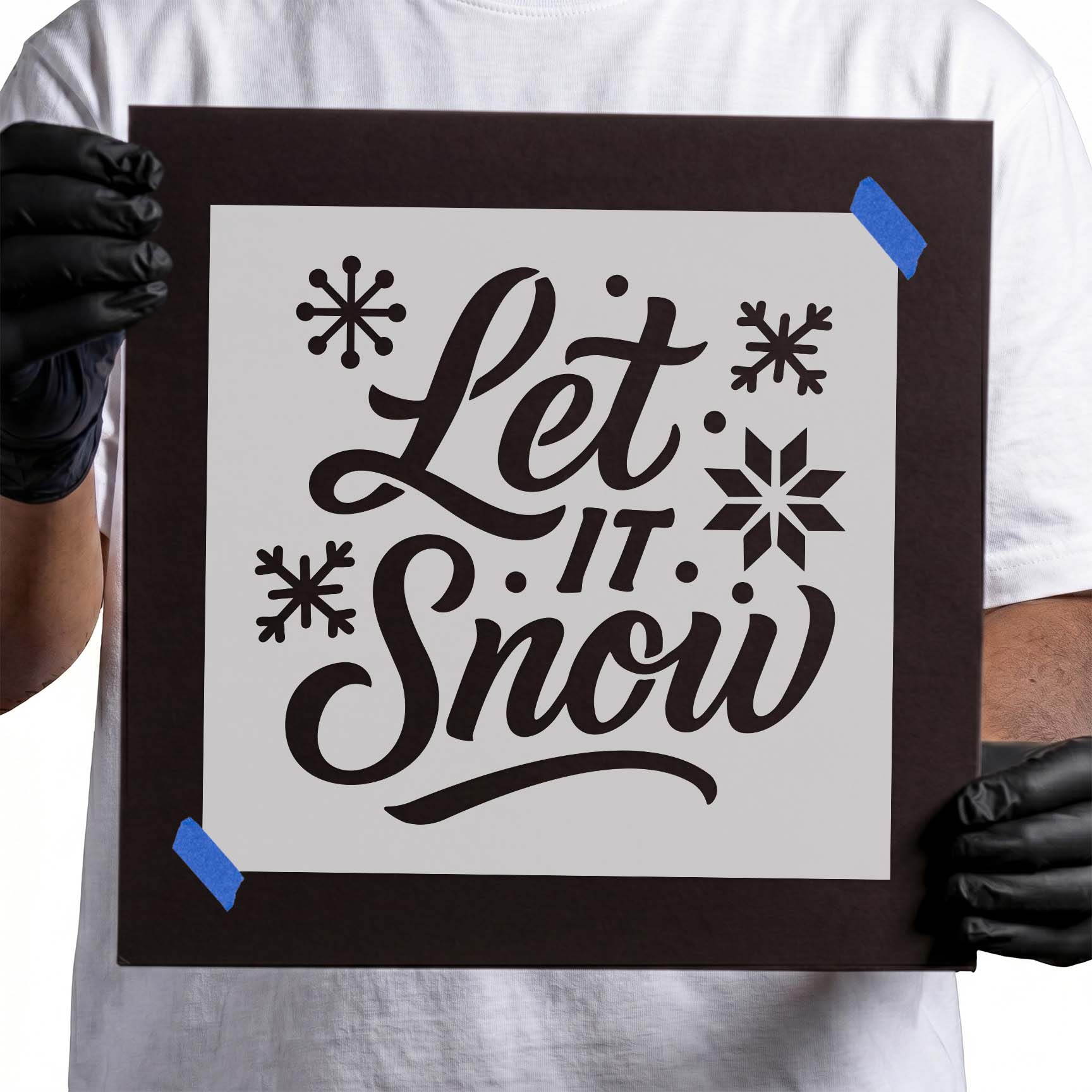 Person holding Festive Let It Snow Text Stencil taped to cardboard