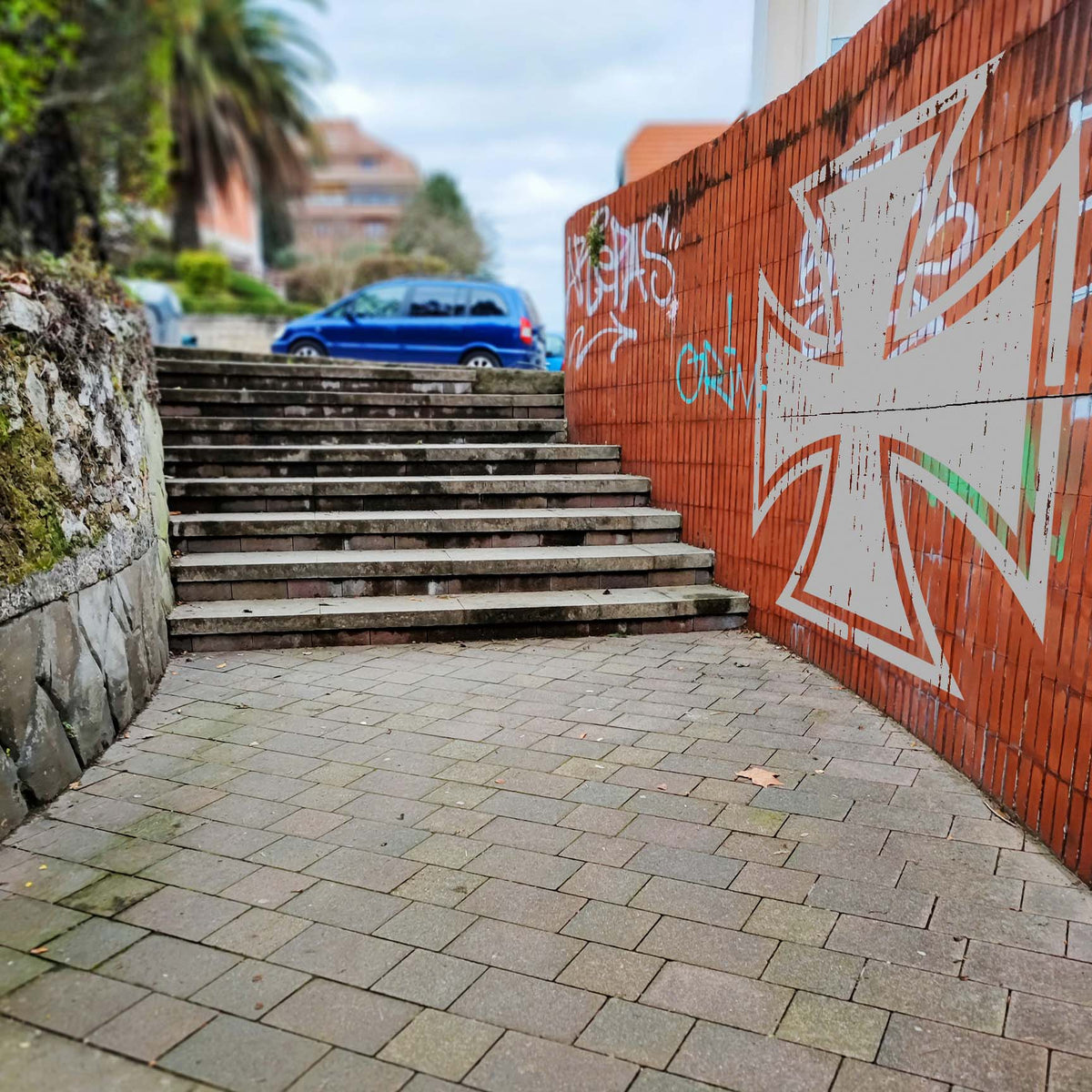 Oversized white Iron Cross Stencil painted on a red brick wall beside outdoor stairs