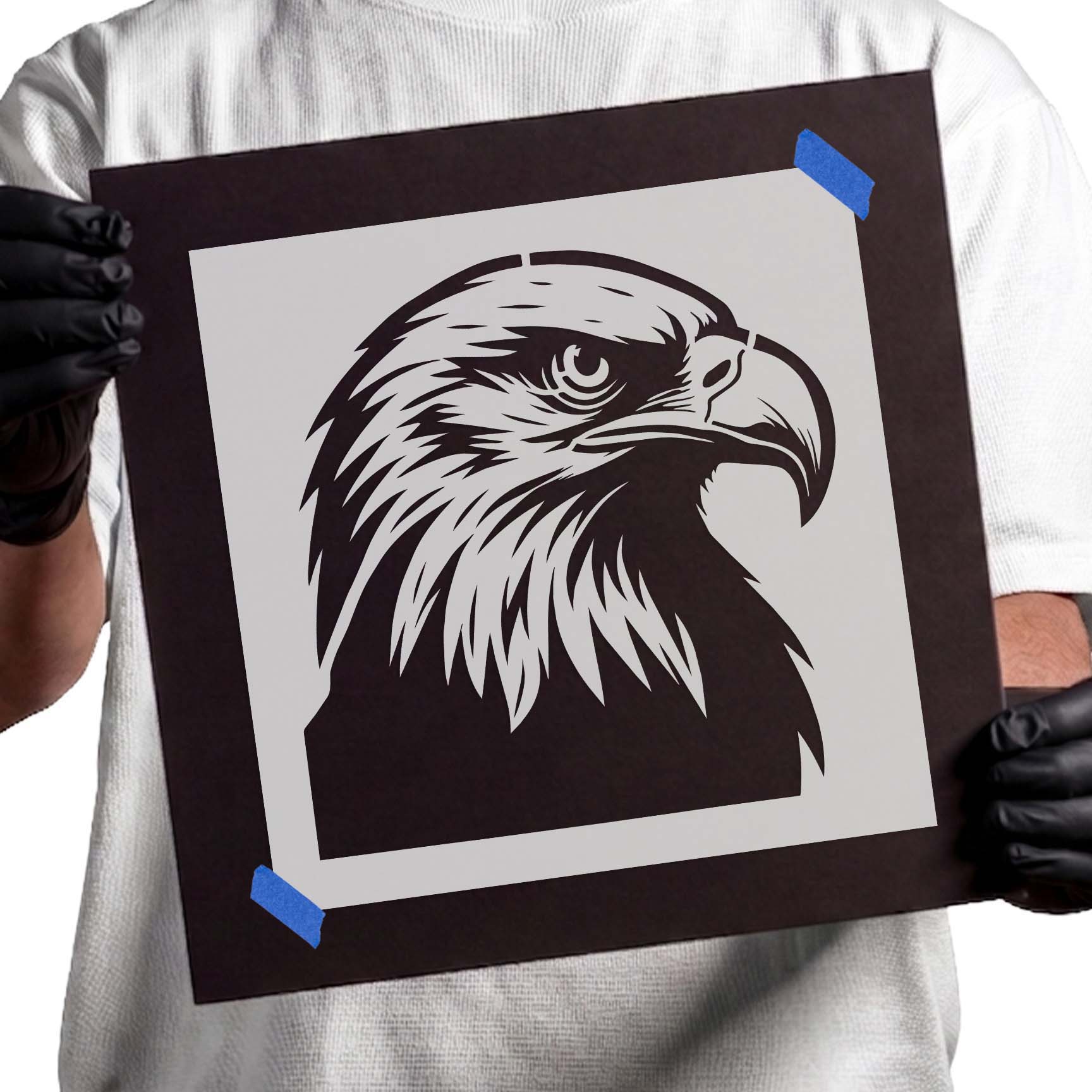 Gloved hands holding Majestic Bald Eagle Head Stencil taped to black cardboard