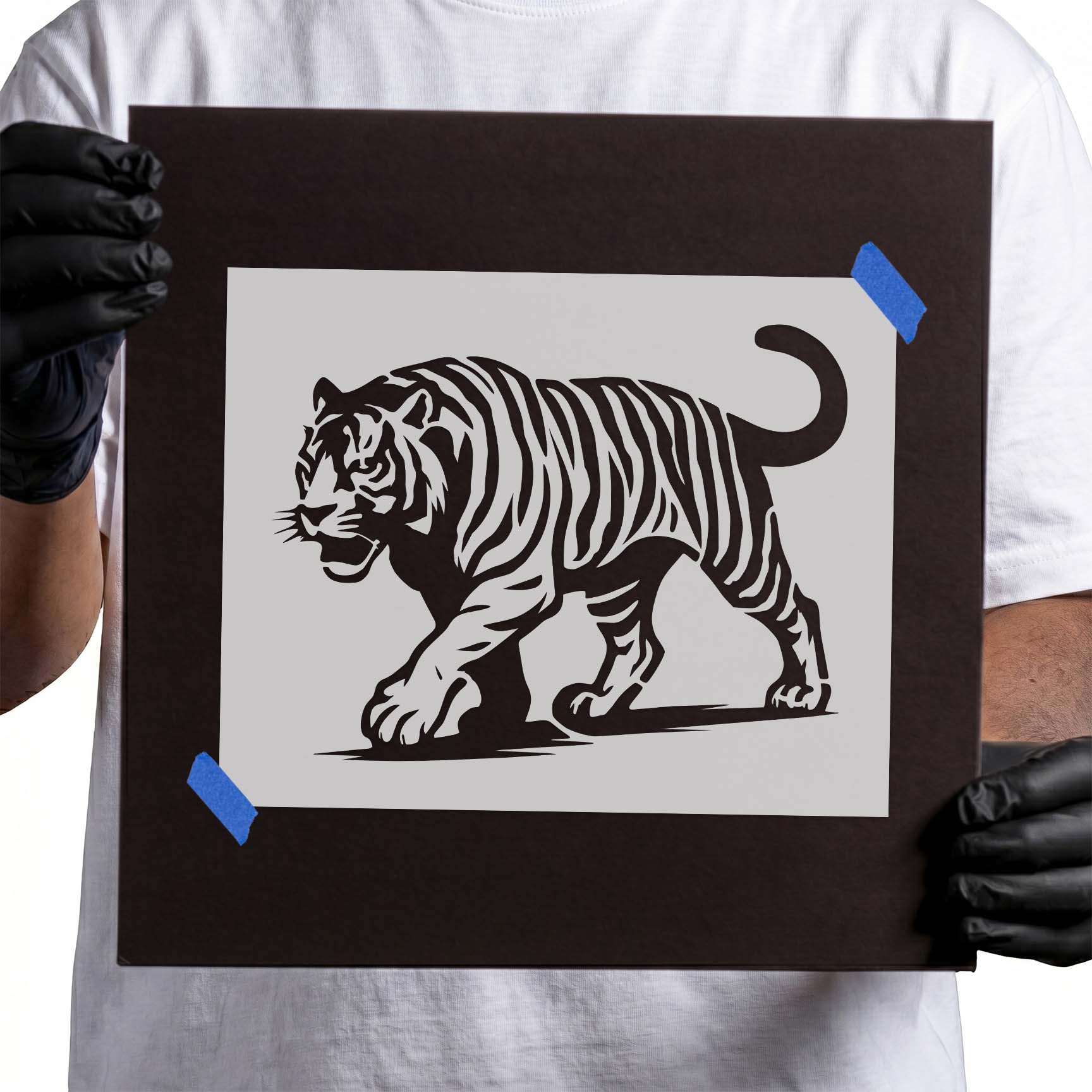 Gloved hands holding Majestic Walking Tiger Stencil taped to cardboard