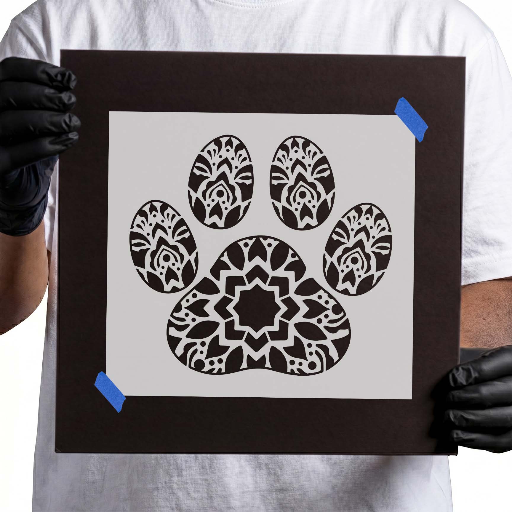 Gloved hands holding Mandala Paw Print Stencil taped to cardboard