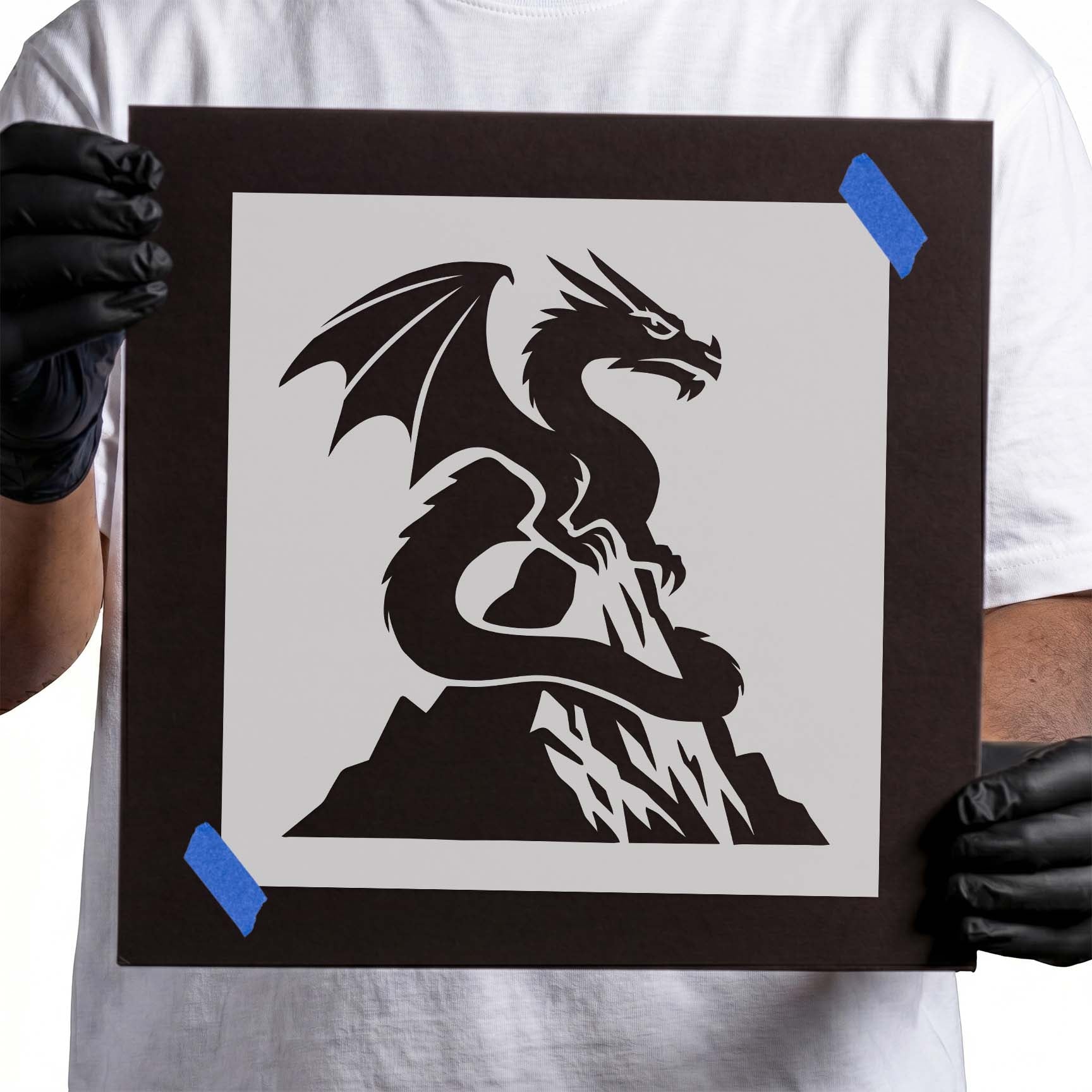 Person holding Mountain Peak Dragon stencil taped to black cardboard