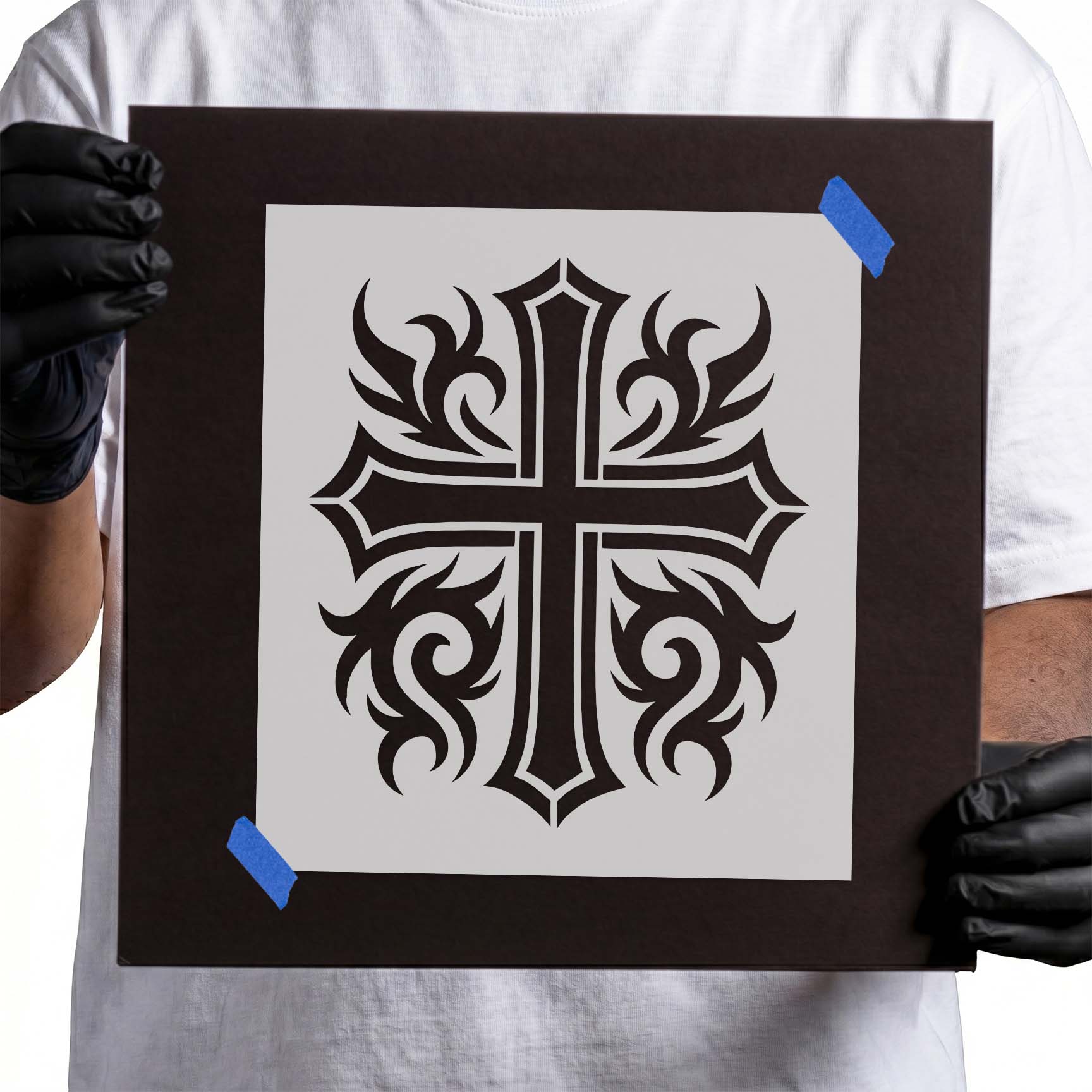 Person holding Ornate Tribal Cross Stencil taped to black cardboard