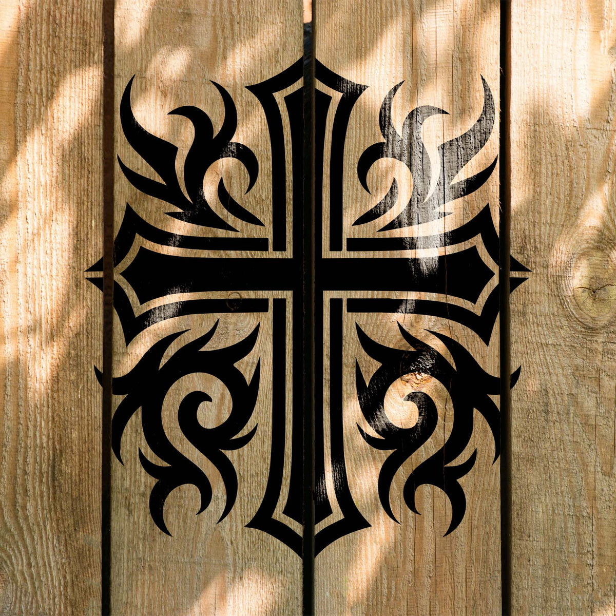 Across rustic wood planks, a black Ornate Tribal Cross Stencil displays sharp swirling accents