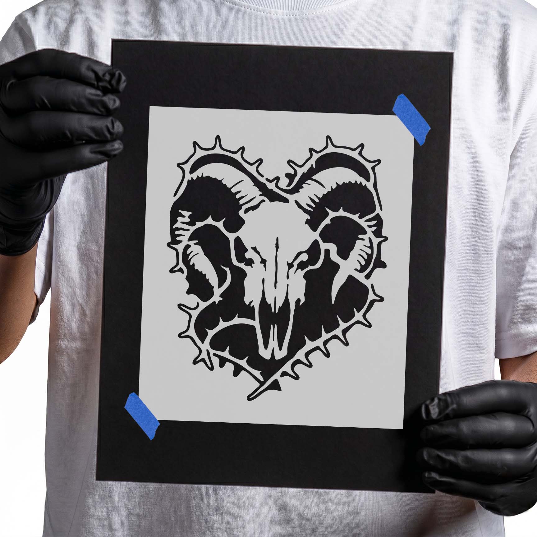 Person holding Ram Skull Thorn Wreath Stencil taped to black cardboard