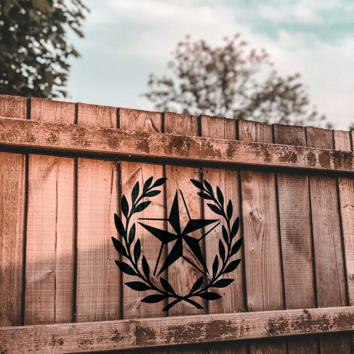 Rustic Star Laurel Wreath Stencil stands out in black against a warm rustic wood fence