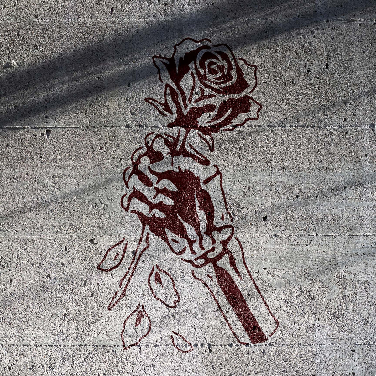 Skeleton Hand Holding Rose Stencil painted deep red across a shadowed concrete wall
