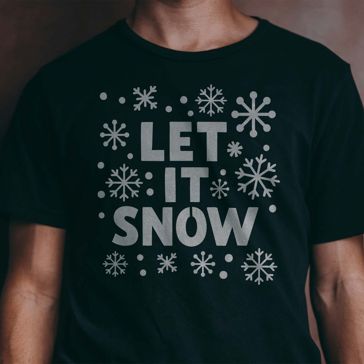 Silver Snowflake Let It Snow Stencil fills a black shirt with bold text and assorted snowflakes.