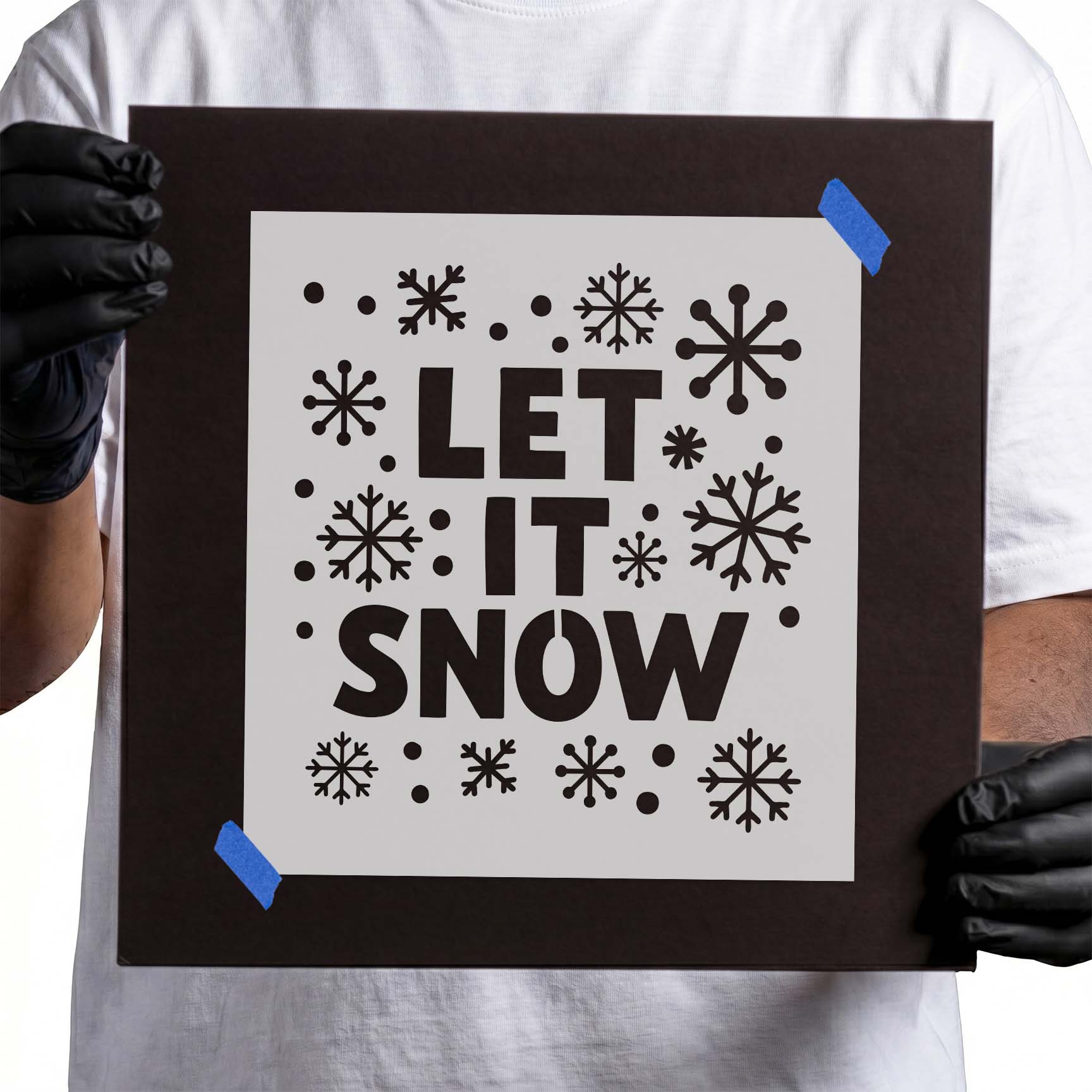 Person holding Snowflake Let It Snow Stencil taped to cardboard