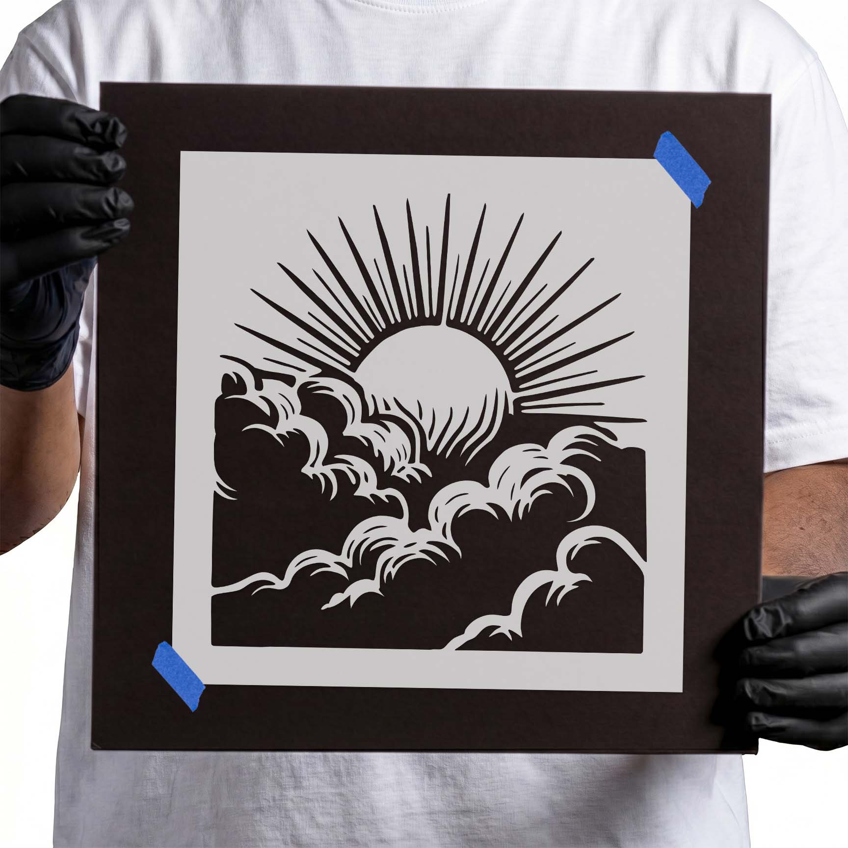 Gloved hands holding Sunrise Above Clouds stencil taped to black cardboard