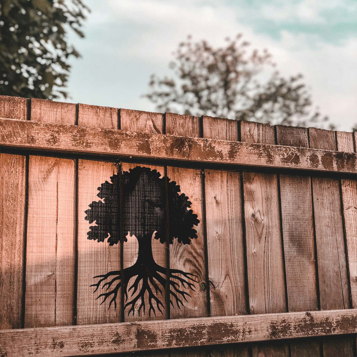 Deep-rooted tree stencil creating a dramatic silhouette across rustic wood fencing