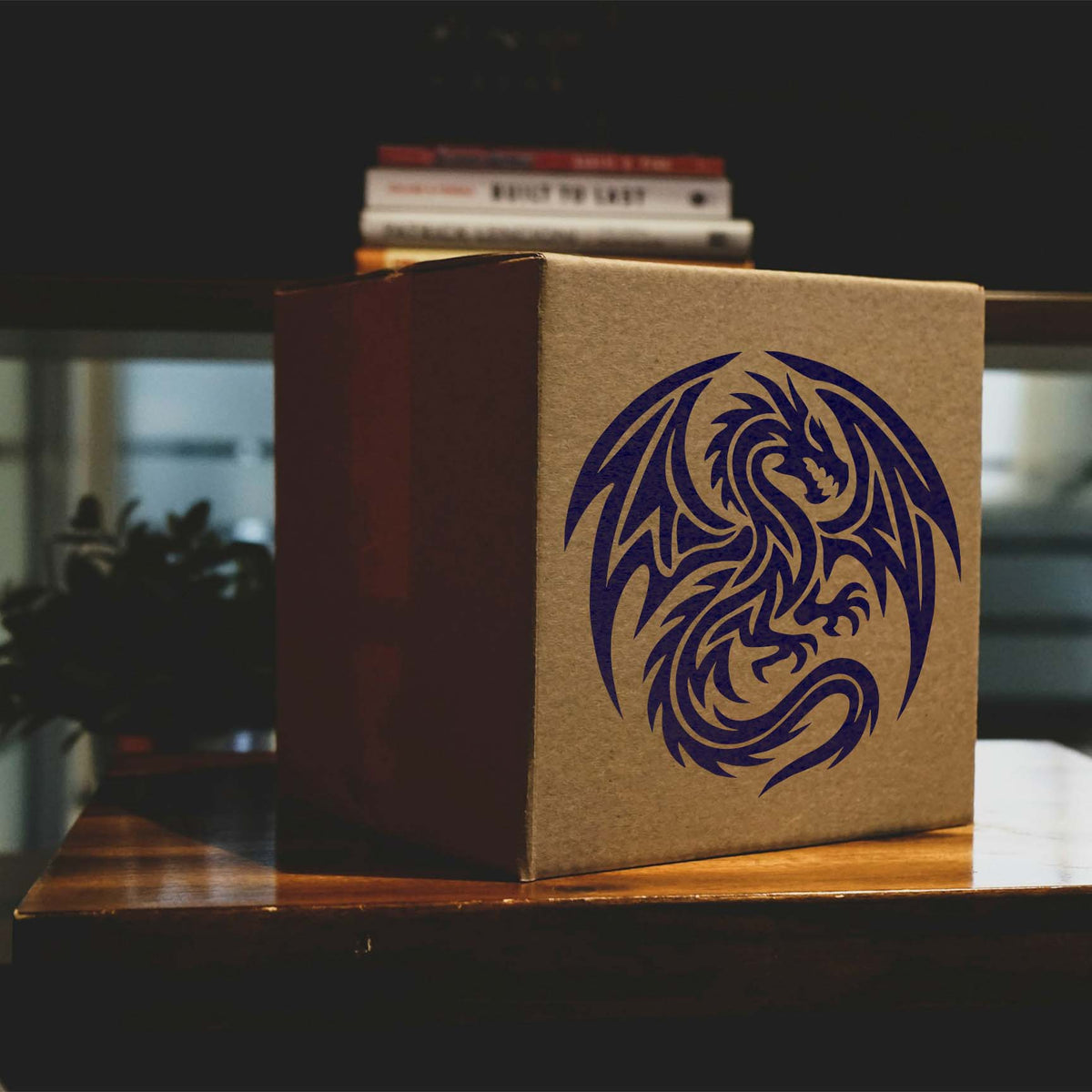 A navy blue Tribal Winged Dragon Stencil features curved wings and a coiled tail on a brown cardboard box.