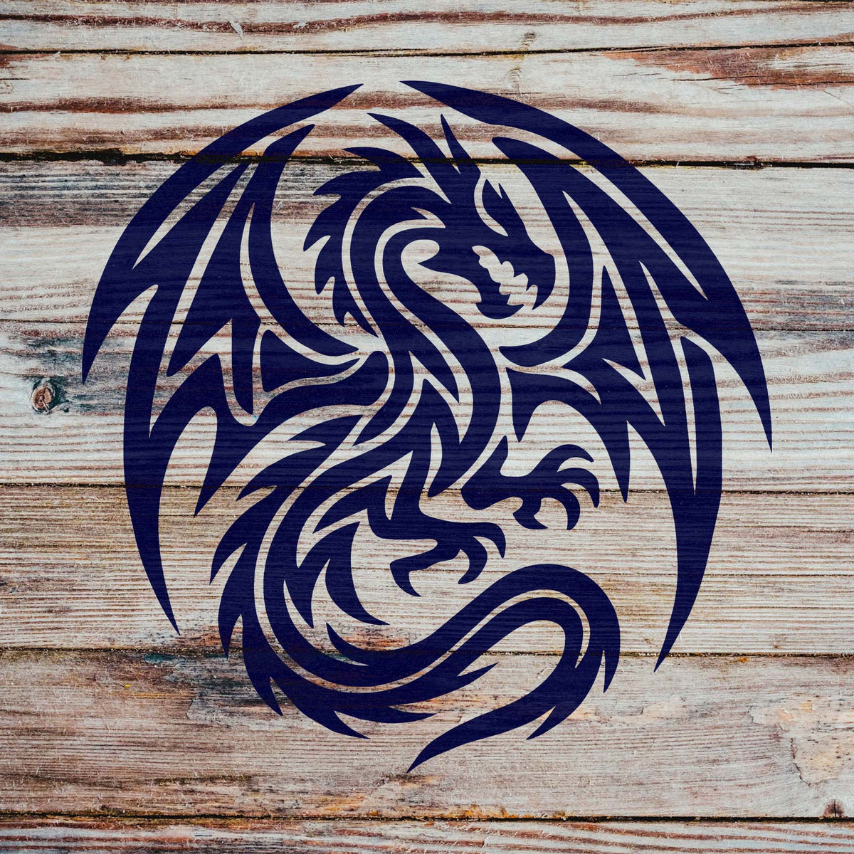 Across weathered wooden planks, the Tribal Winged Dragon Stencil reveals a horned dragon in bold navy blue.