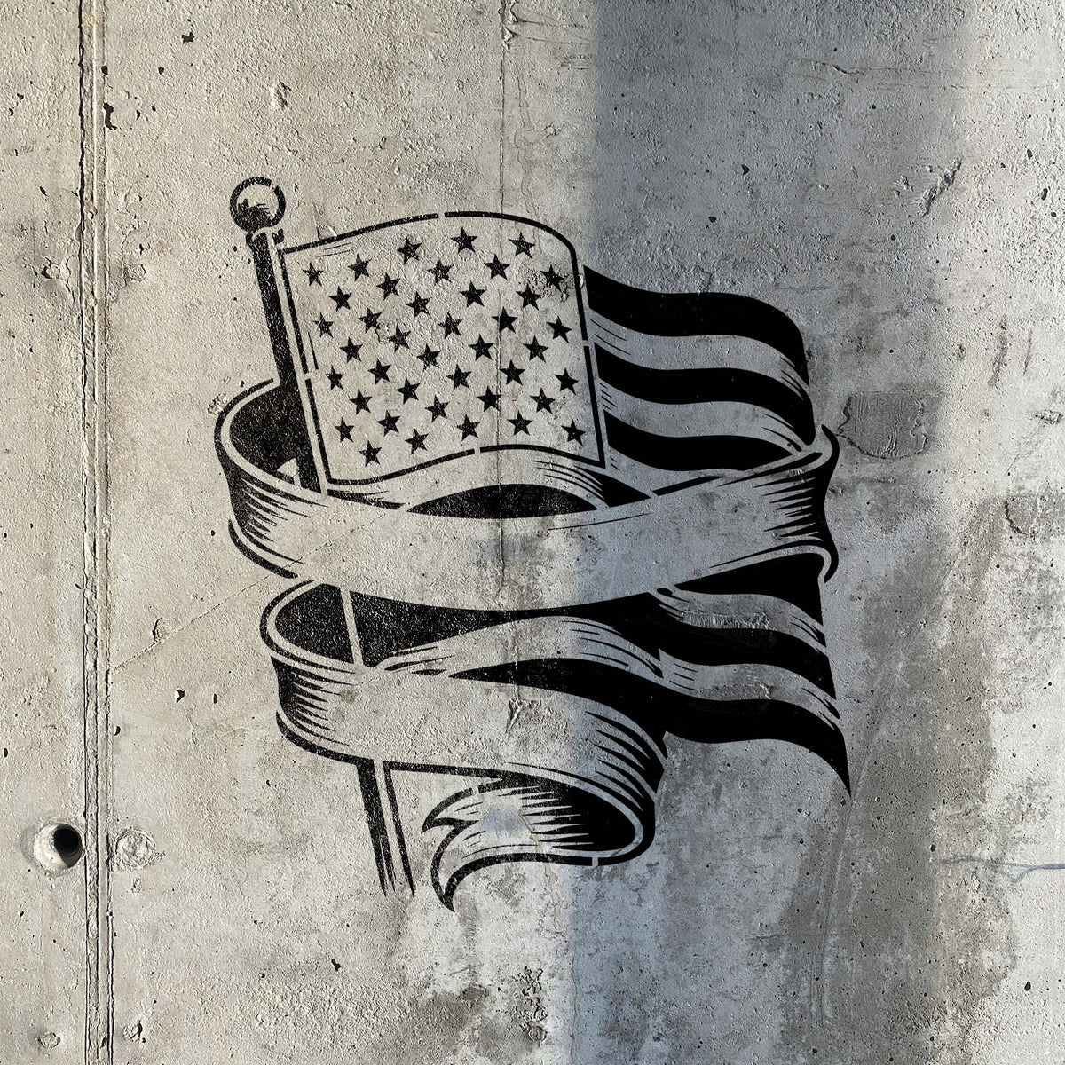 Weathered concrete displays the American Flag Banner Stencil with bold stars, stripes, and ribbons