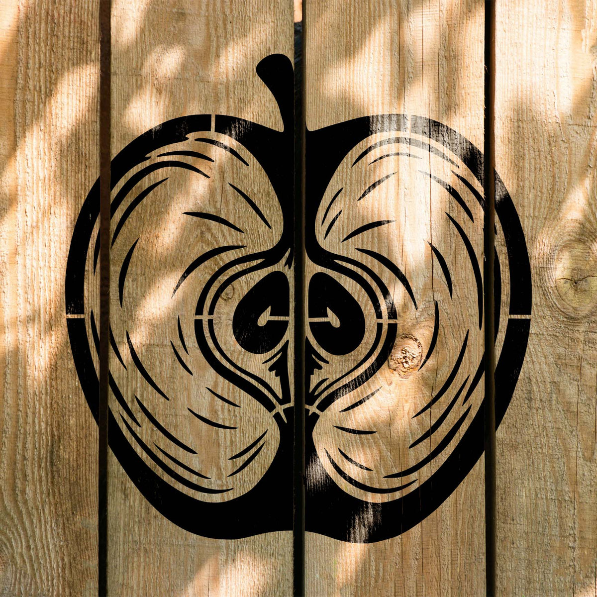 Across sunlit wooden planks, the Apple Cross Section Stencil displays a black sliced apple design.