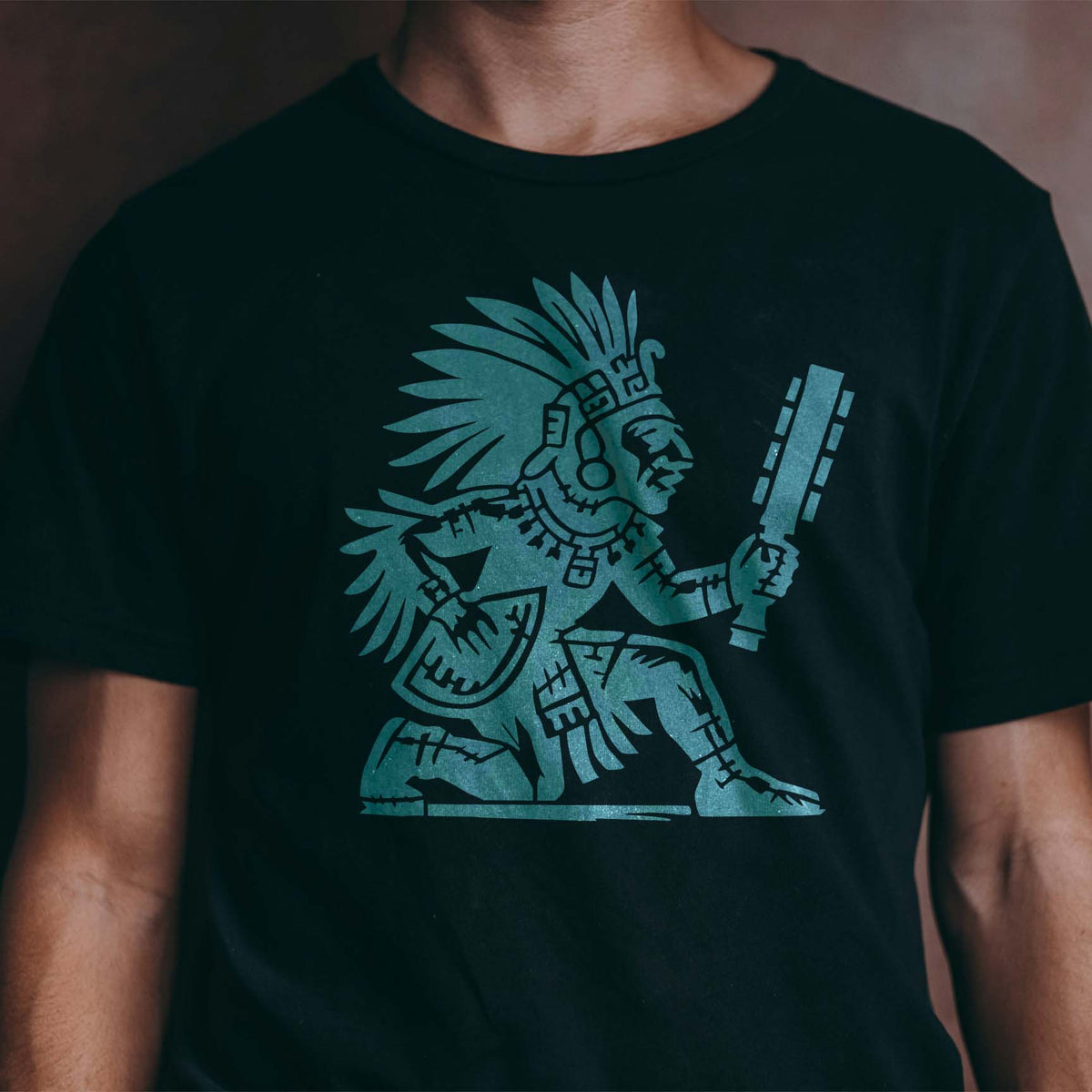 Aztec Warrior Stencil printed in teal on the front of a black T-shirt.