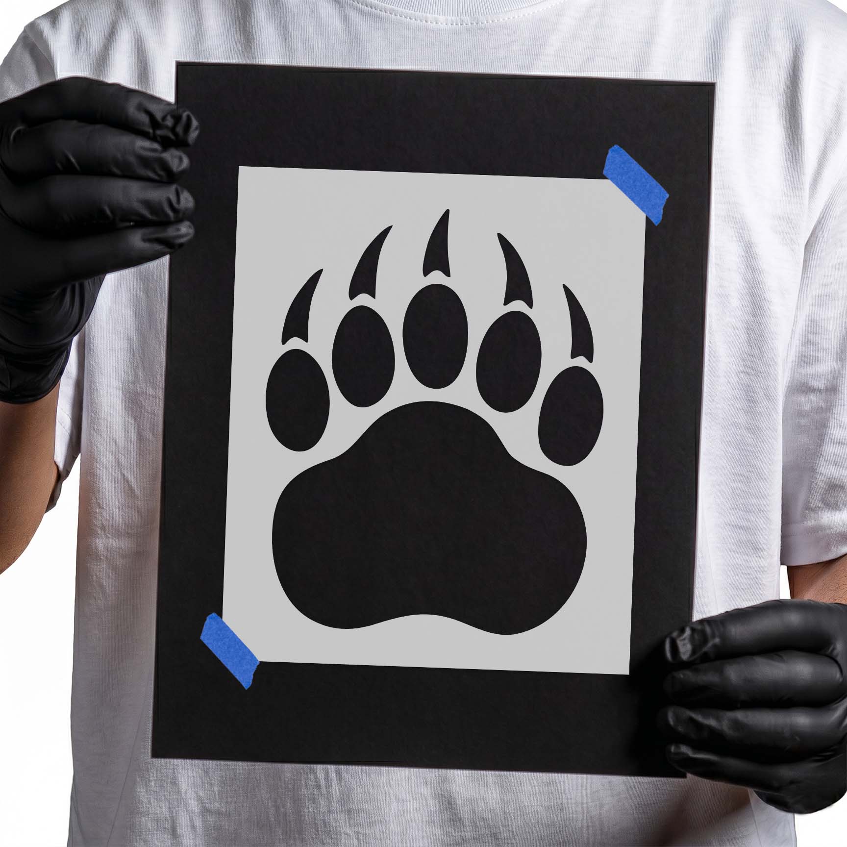 Gloved hands holding Bear Paw Print Stencil taped to black cardboard