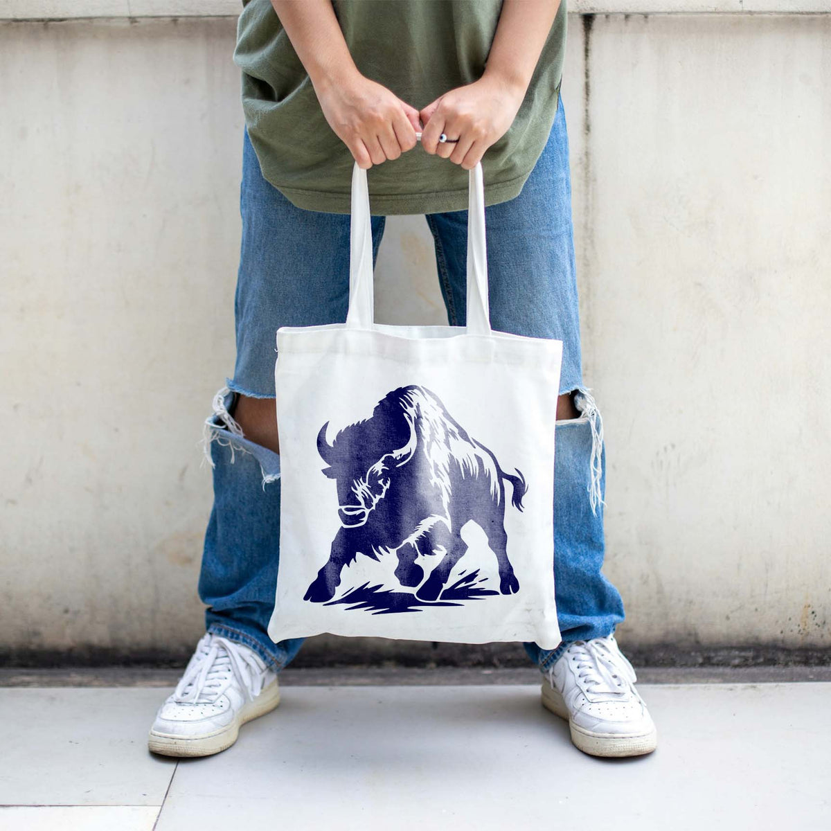 Stampeding Bison Stencil painted navy on a white tote bag held by a person in casual clothing.