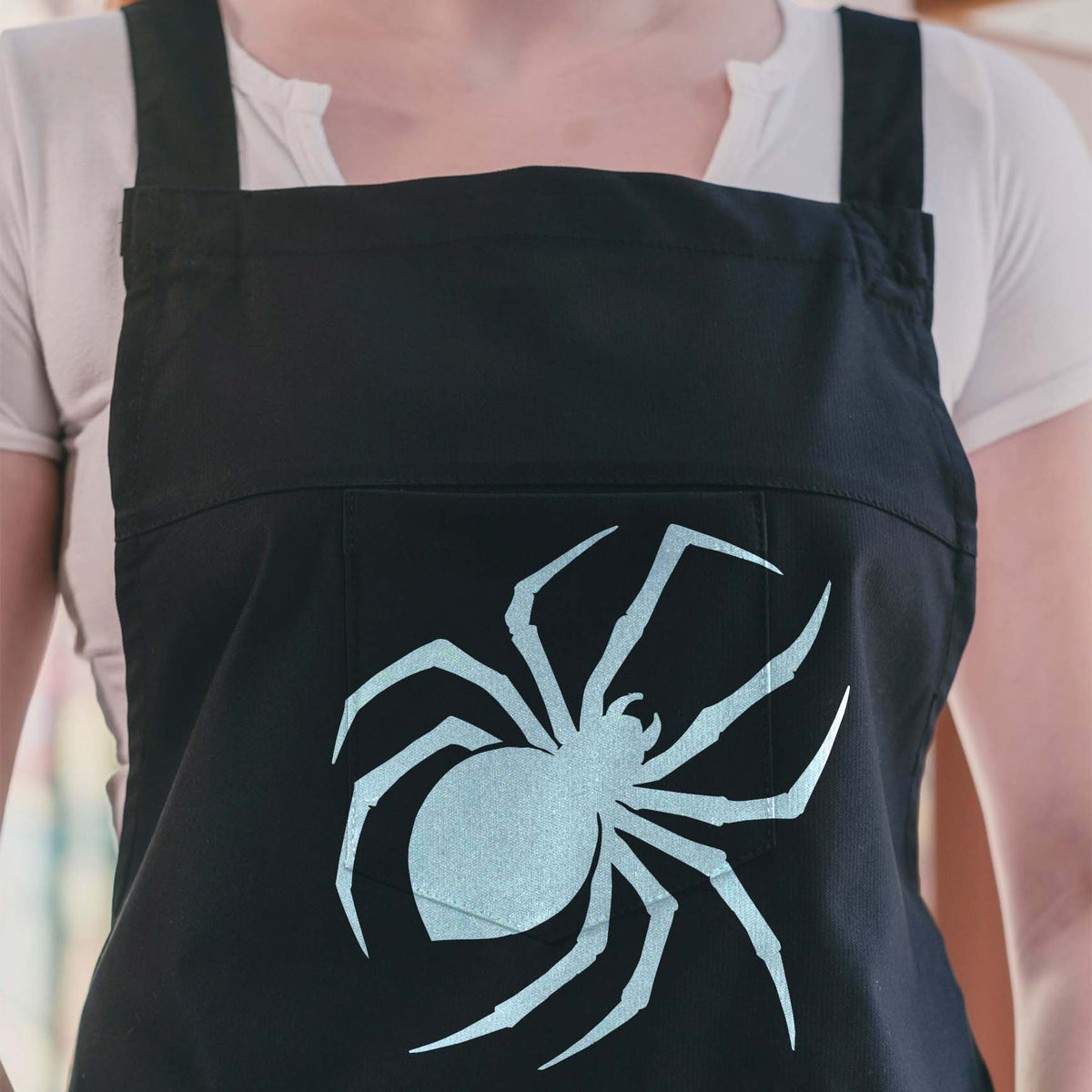 Black Widow Spider Silhouette Stencil stands out in silver across a dark apron