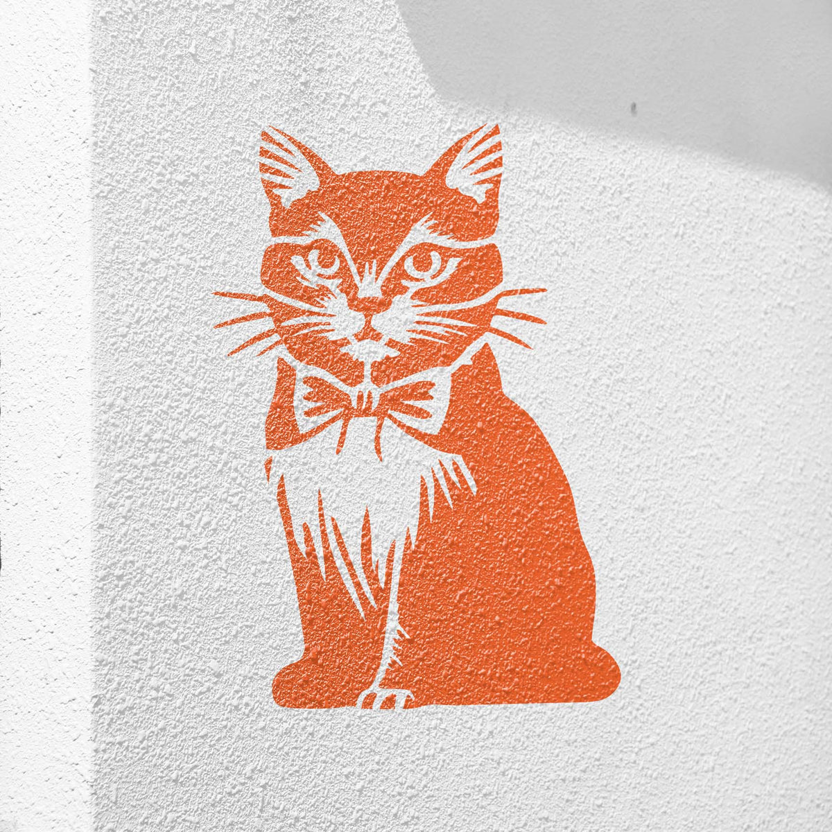Bright orange Bow Tie Cat Stencil art brings a charming cat portrait with a bow tie to a white stucco wall.
