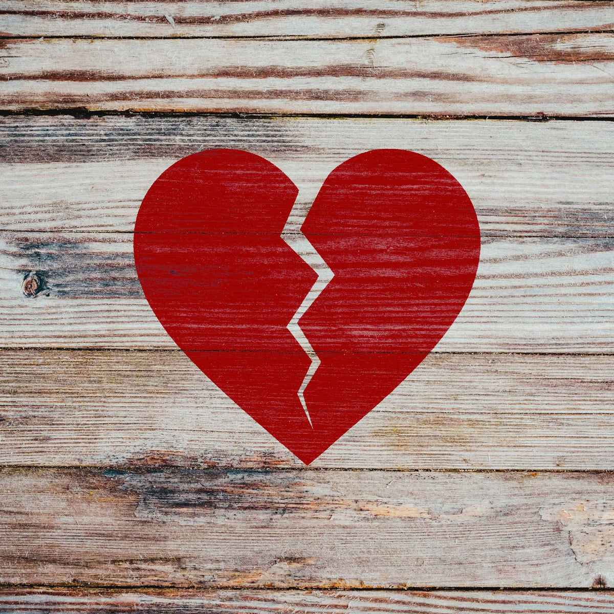 Rustic wood displays the Broken Heart Crack Stencil as a distressed red heart with a jagged split