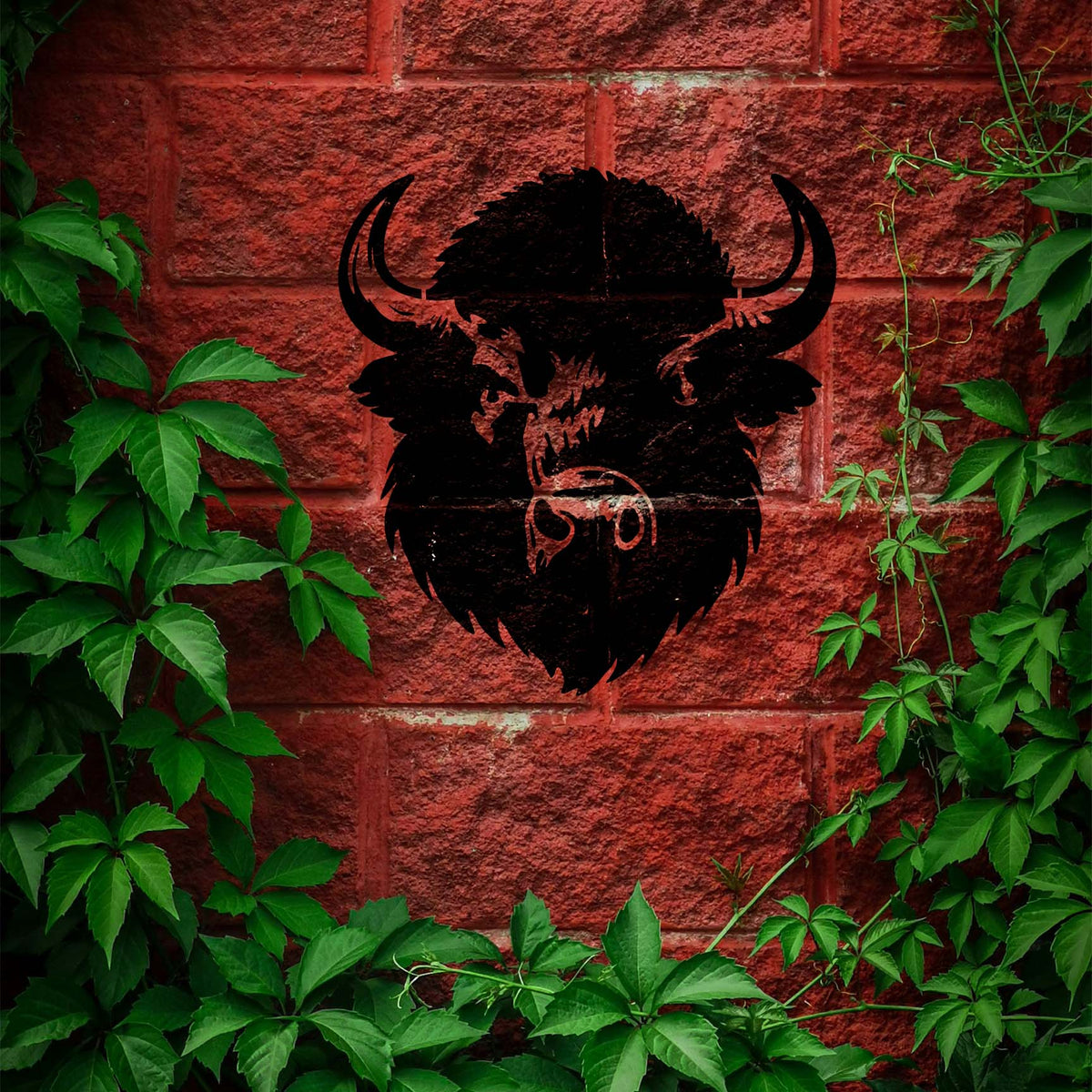 Shaggy Buffalo Head Stencil painted black on a red brick wall surrounded by green climbing vines.