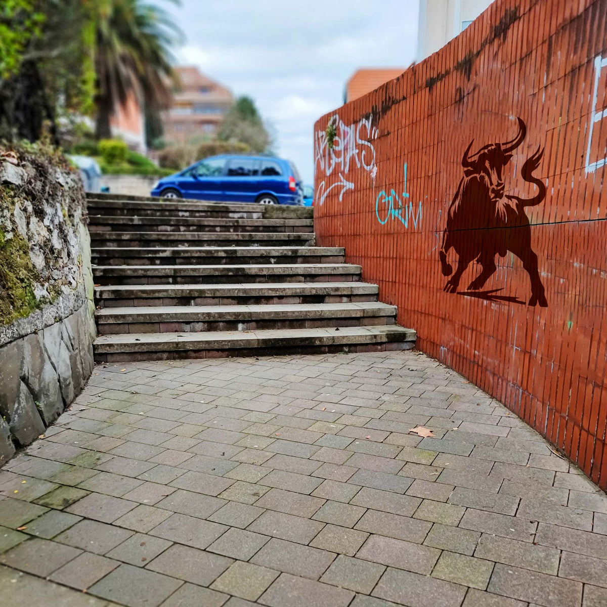 Charging Bull Stencil displayed on a red brick wall beside an outdoor stairway.