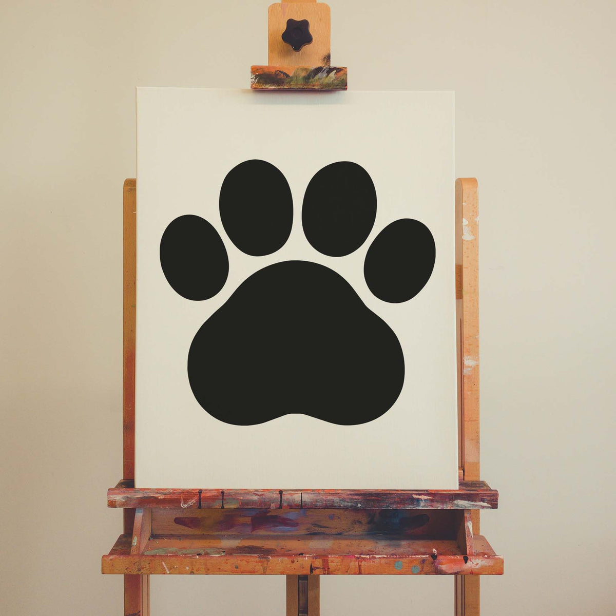 Cartoon Paw Print Stencil displayed as black paw artwork on a canvas set on an easel.
