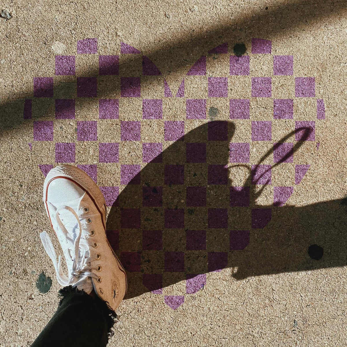 On sunlit pavement, Checkerboard Heart Stencil forms a purple heart beneath a white sneaker.