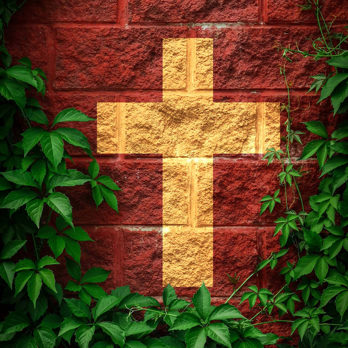 A golden Classic Christian Cross Silhouette Stencil stands out on a red brick wall surrounded by ivy.