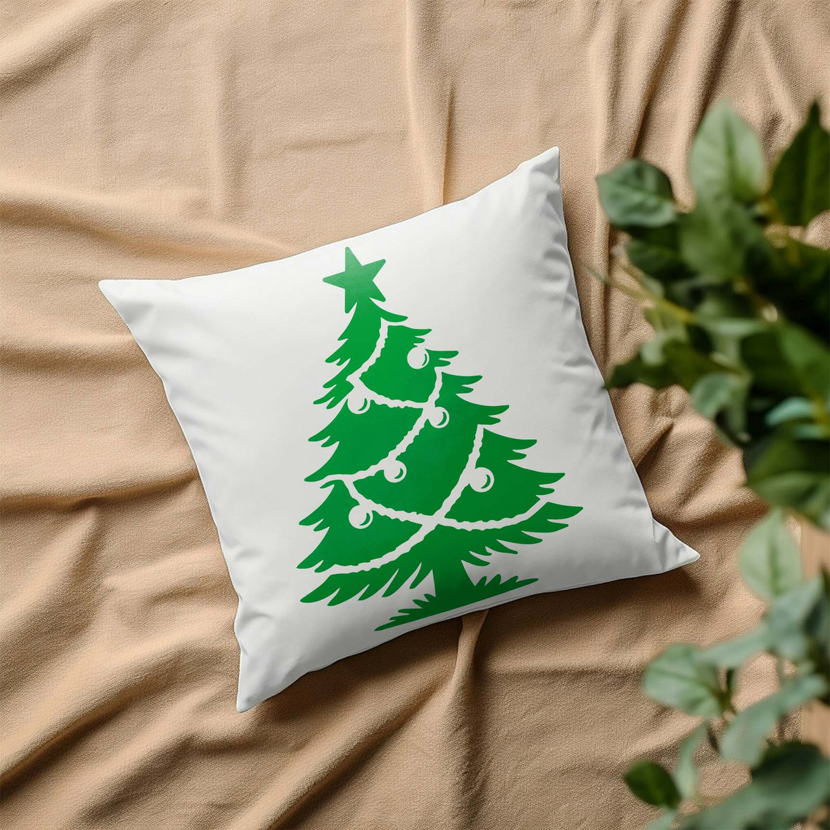 White pillow featuring the Classic Decorated Christmas Tree Stencil on draped beige fabric.
