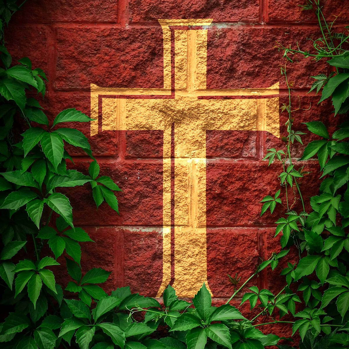 Framed by lush green vines, the Classic Latin Cross Stencil shines in gold against a textured red brick wall.