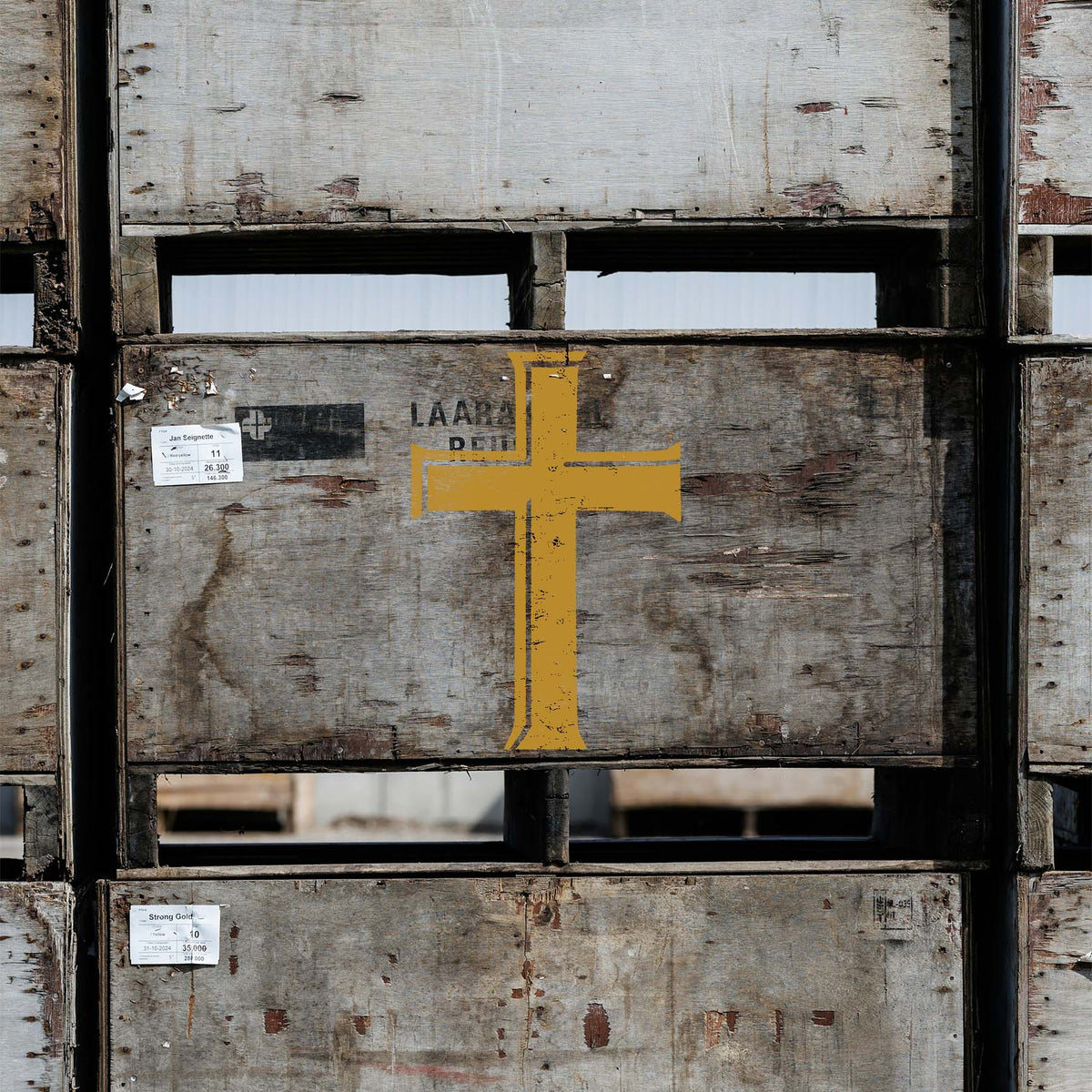 A weathered wooden crate displays the Classic Latin Cross Stencil in rustic golden yellow with a vintage finish.