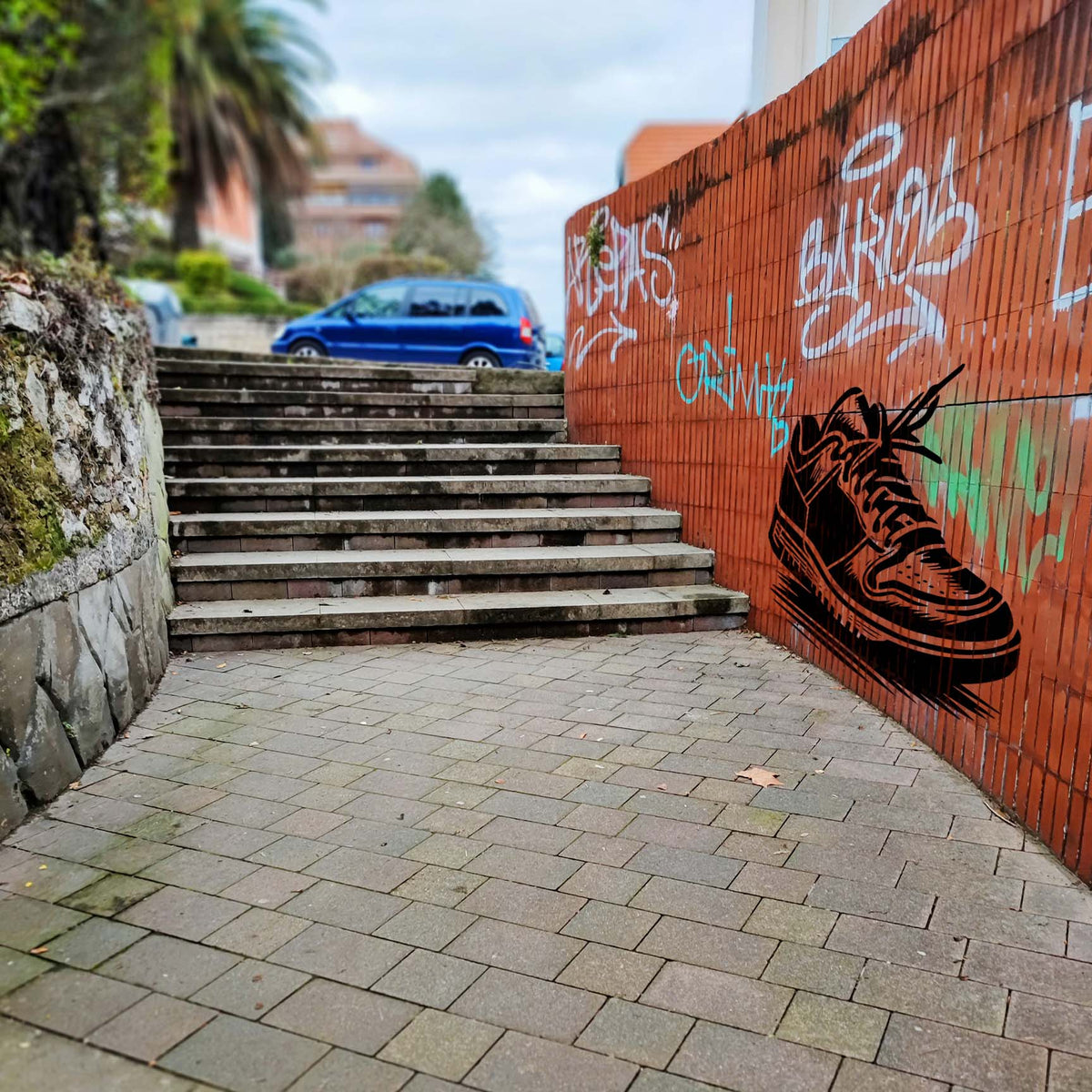 Against a graffiti-covered brick wall, the Classic Low Top Sneaker Stencil displays a black lace-up shoe.