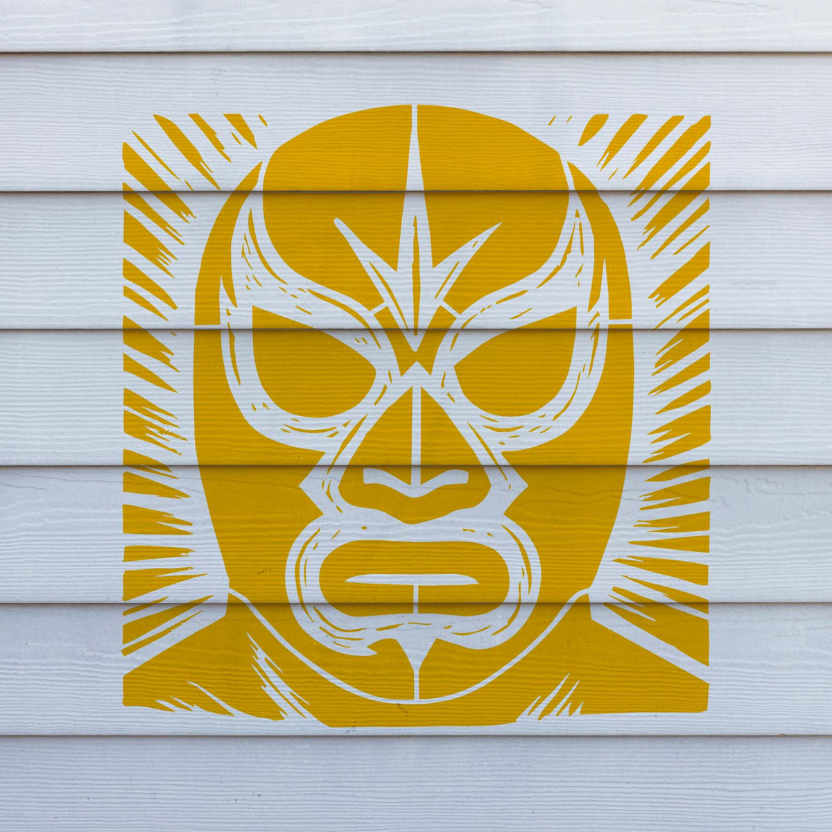 Across white horizontal siding, the Classic Lucha Libre Wrestling Mask Stencil reveals a striking yellow masked face.