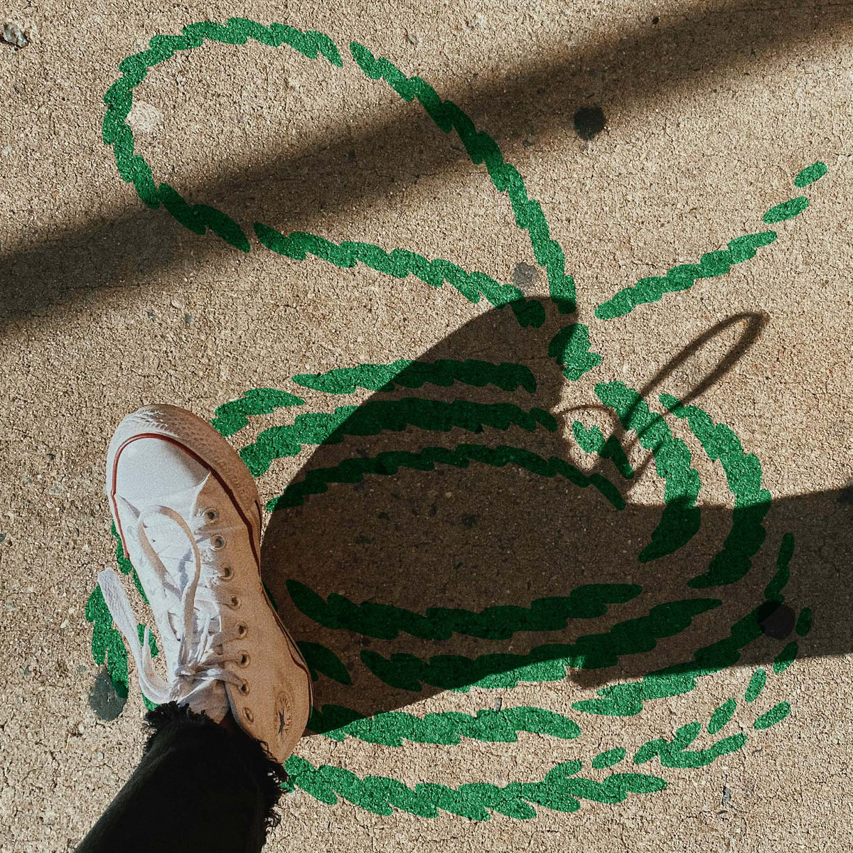Across a sunlit concrete sidewalk, the Coiled Lasso Stencil displays green rope loops beneath bold shadows.