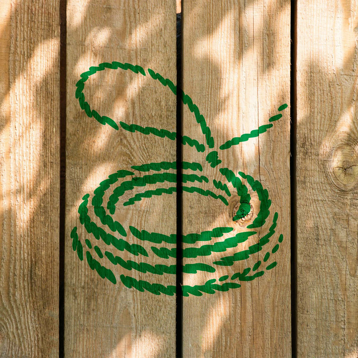A Coiled Lasso Stencil in bright green winds into neat rope loops on sun-dappled wooden fence planks.