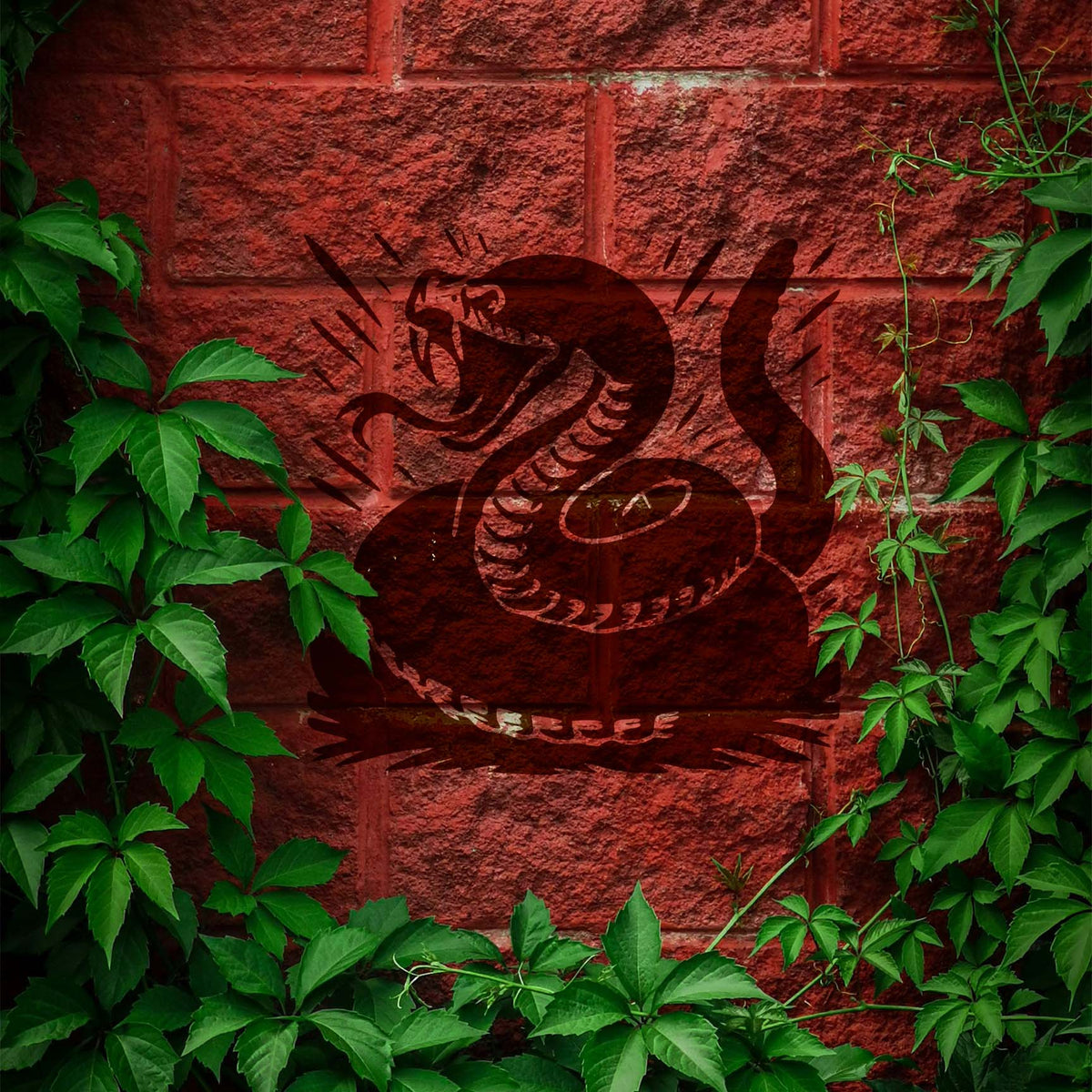 Coiled rattlesnake stencil painted on red brick wall with greenery