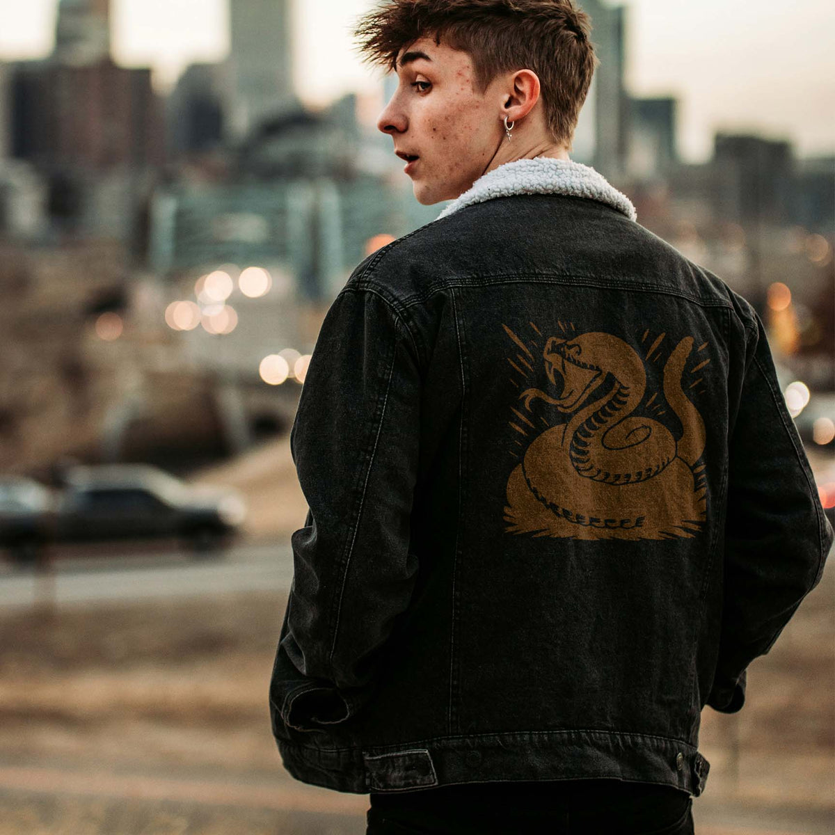 Rearing rattlesnake stencil printed across back of black denim jacket