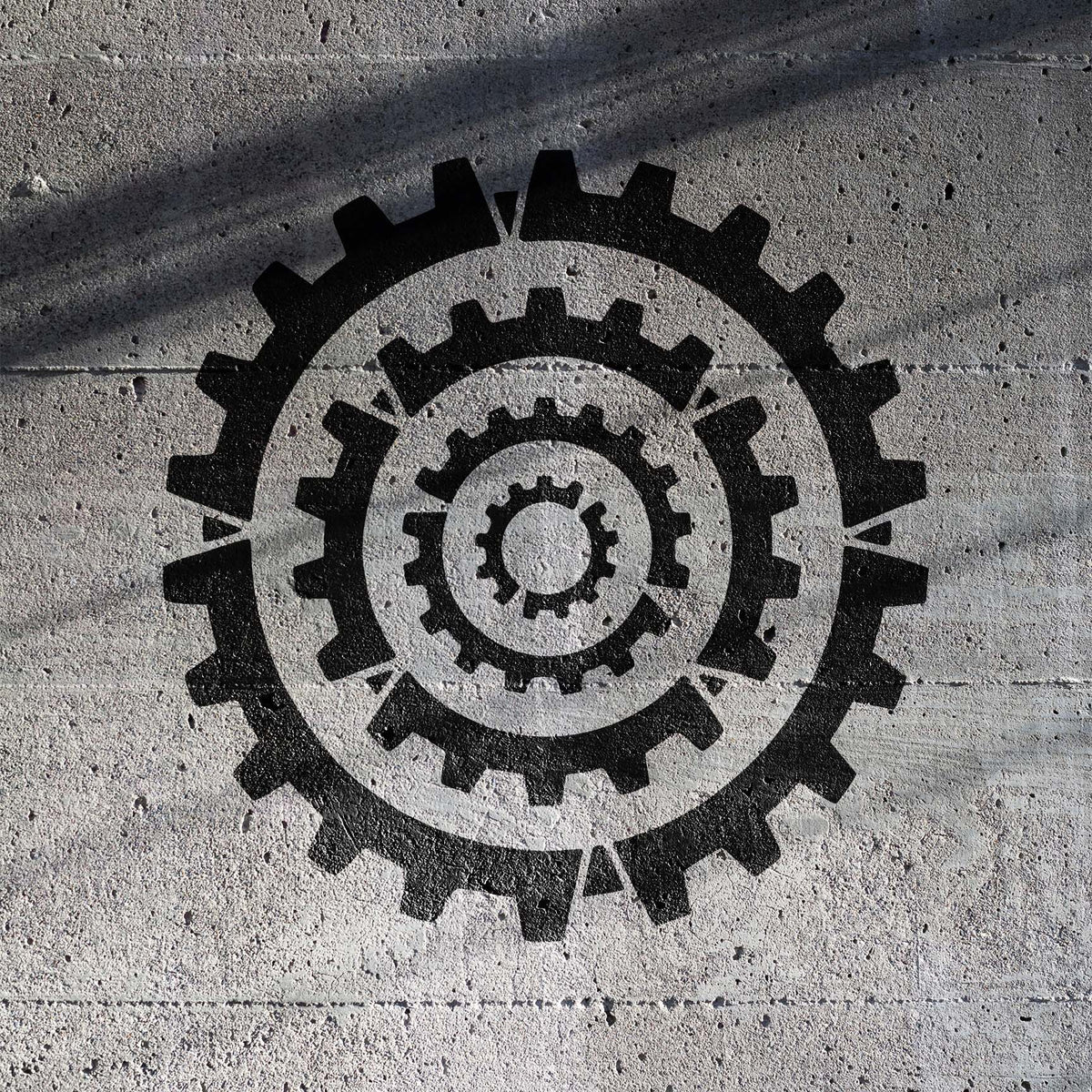 Bold black gears from the Concentric Cogs Stencil form a circular industrial design on textured concrete.