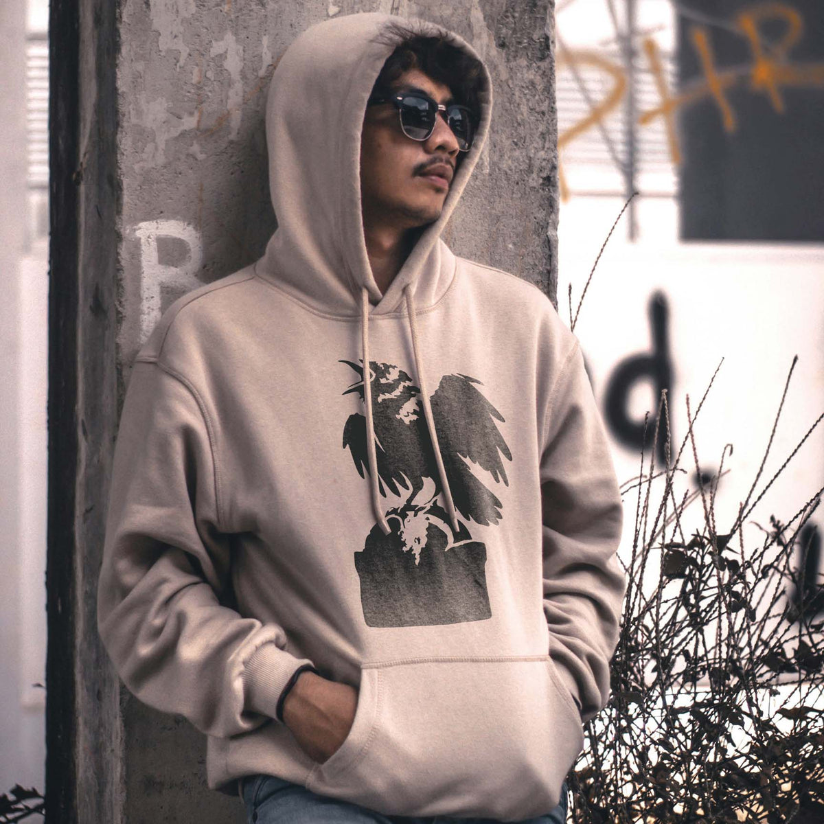Crow on Tombstone Stencil printed on a beige hoodie worn in an urban street scene.