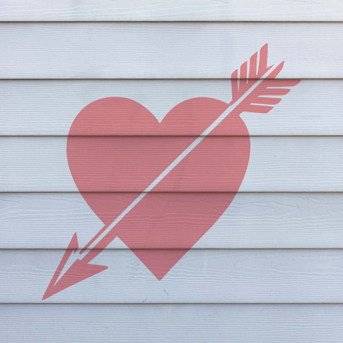Soft pink Cupid Heart with Arrow Stencil spans across clean white horizontal wood siding