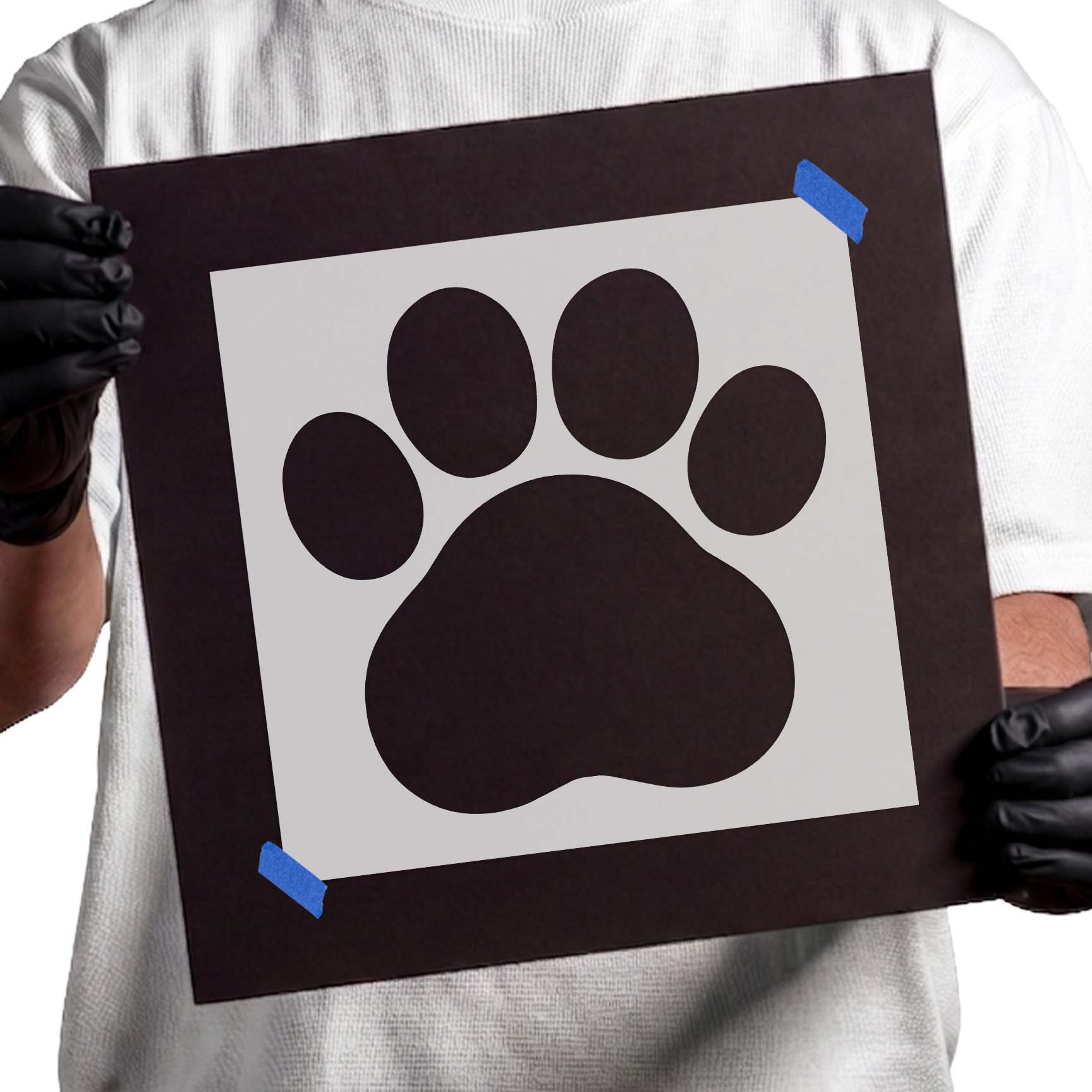 Person holding Cartoon Paw Print stencil taped to black cardboard