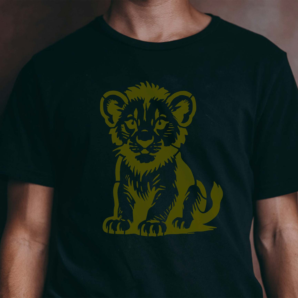 Cute Lion Cub Stencil displays a sweet seated lion cub printed in gold on a black T-shirt.