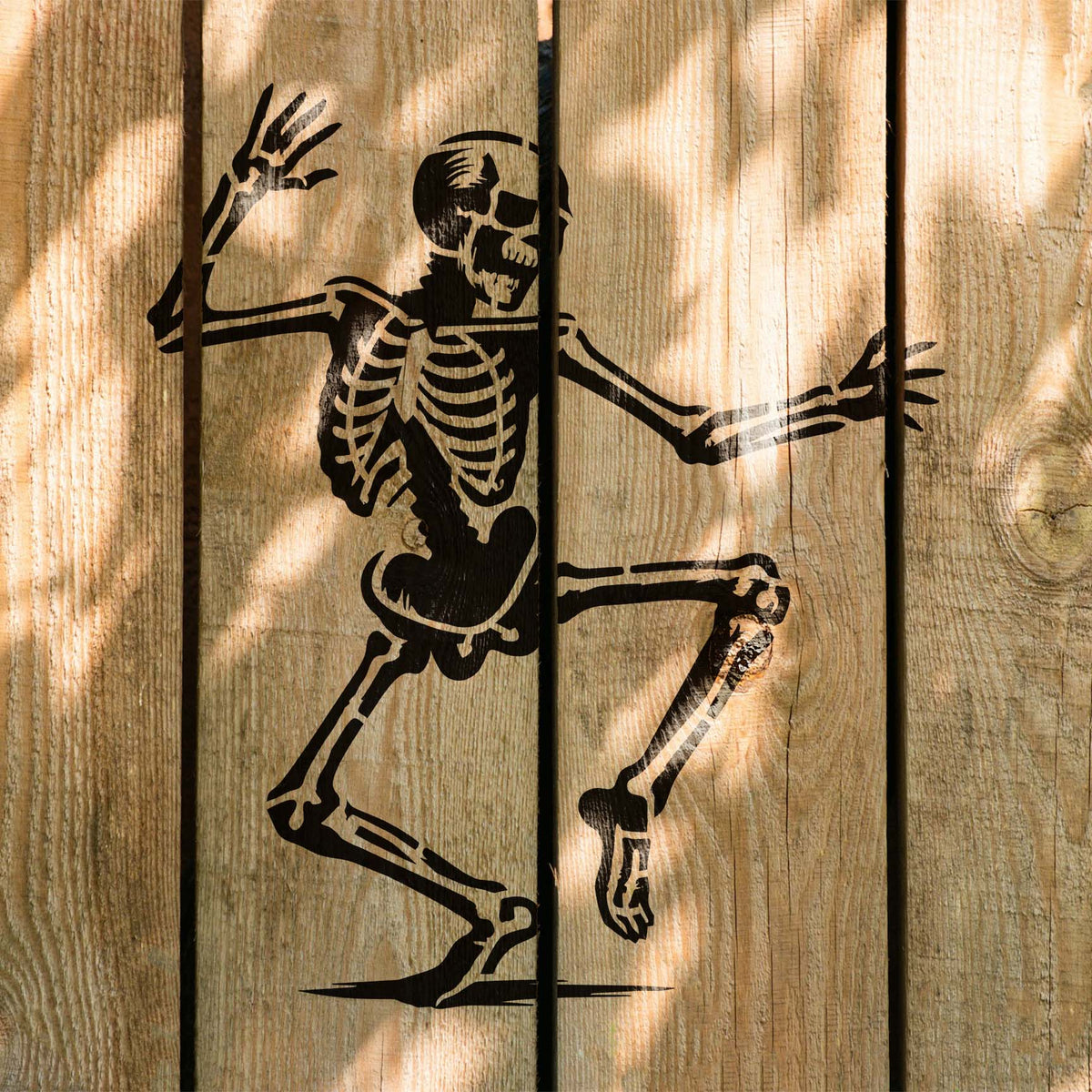 Bold Dancing Skeleton Halloween Stencil sprawls across sunlit wood planks in black paint
