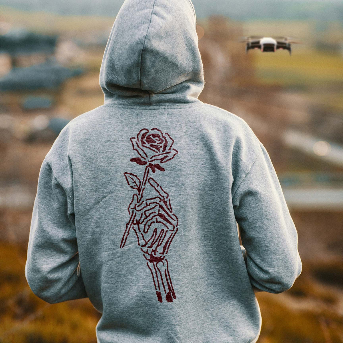 A Death Bouquet Skeleton Hand Stencil adds a dark rose motif to the back of a gray hoodie