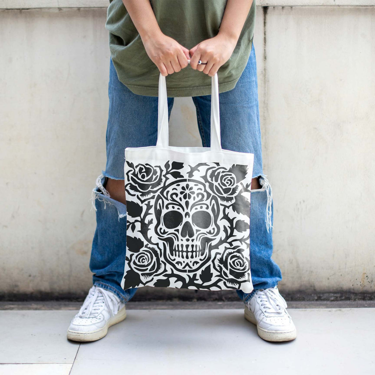 A white tote bag features the Decorative Sugar Skull and Roses Stencil framed by blooming roses